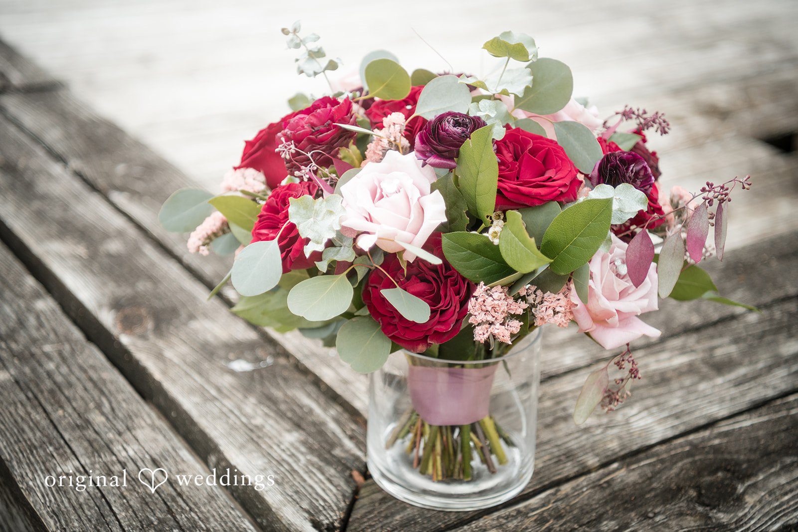 Natalie + Dakin Floral bouquet with red, pink, and white roses in a glass vase on a wooden surface.