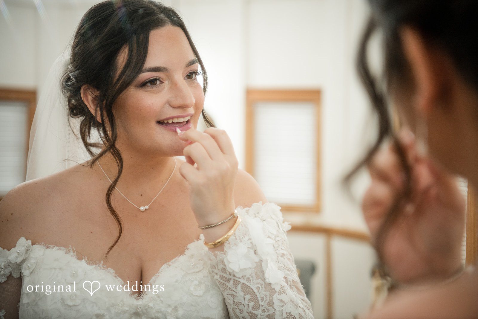 Natalie + Dakin Bride in a lace gown looking at her reflection in a mirror while applying lipstick.