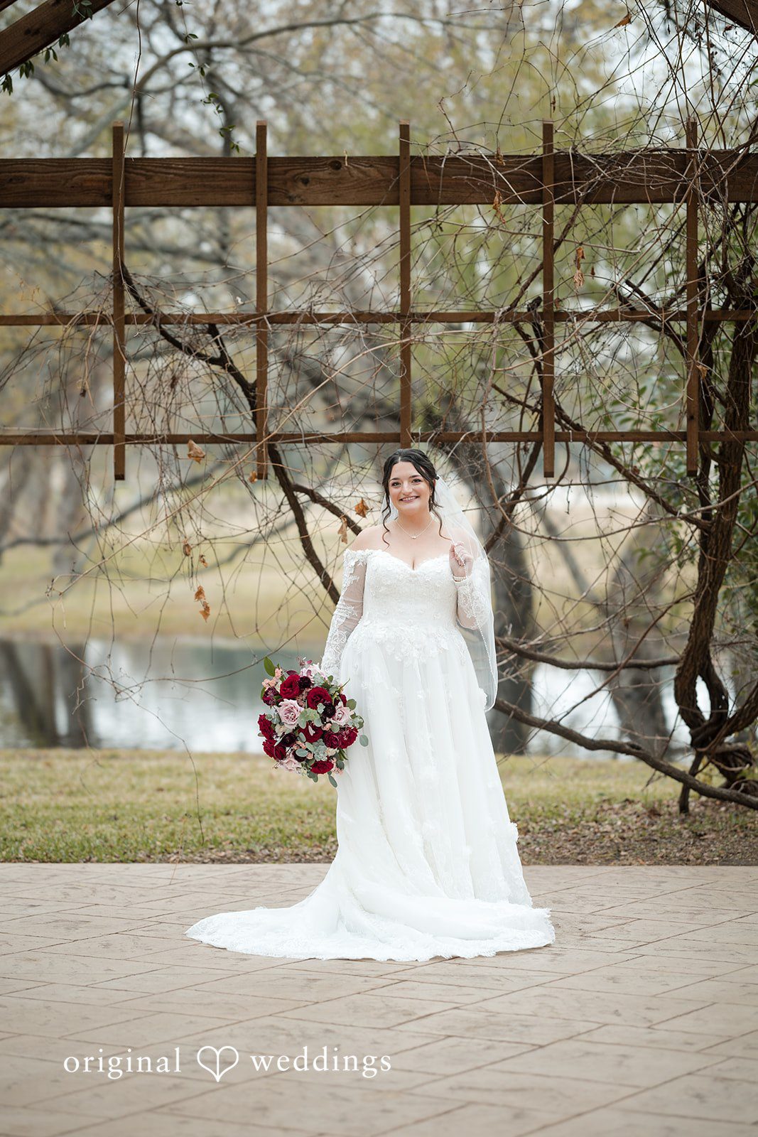 Natalie + Dakin Bride in a long white gown and veil holding a red floral bouquet.