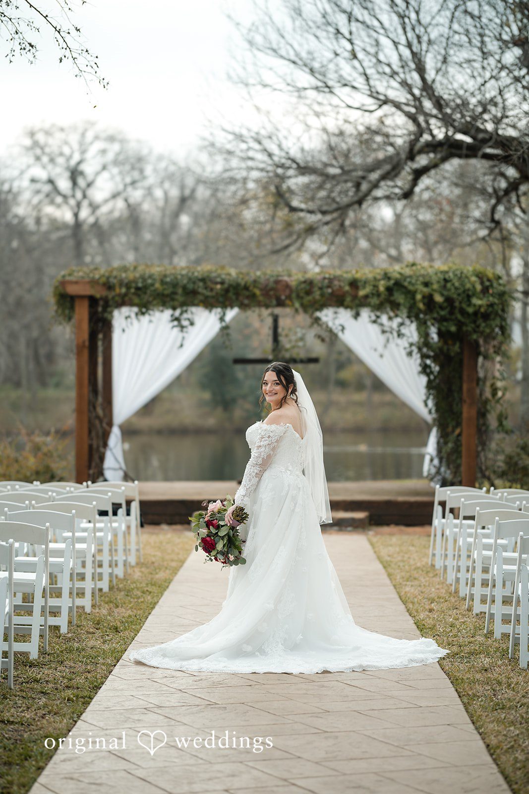 Natalie + Dakin Bride in a white wedding dress walking down a central aisle toward a wooden altar structure.