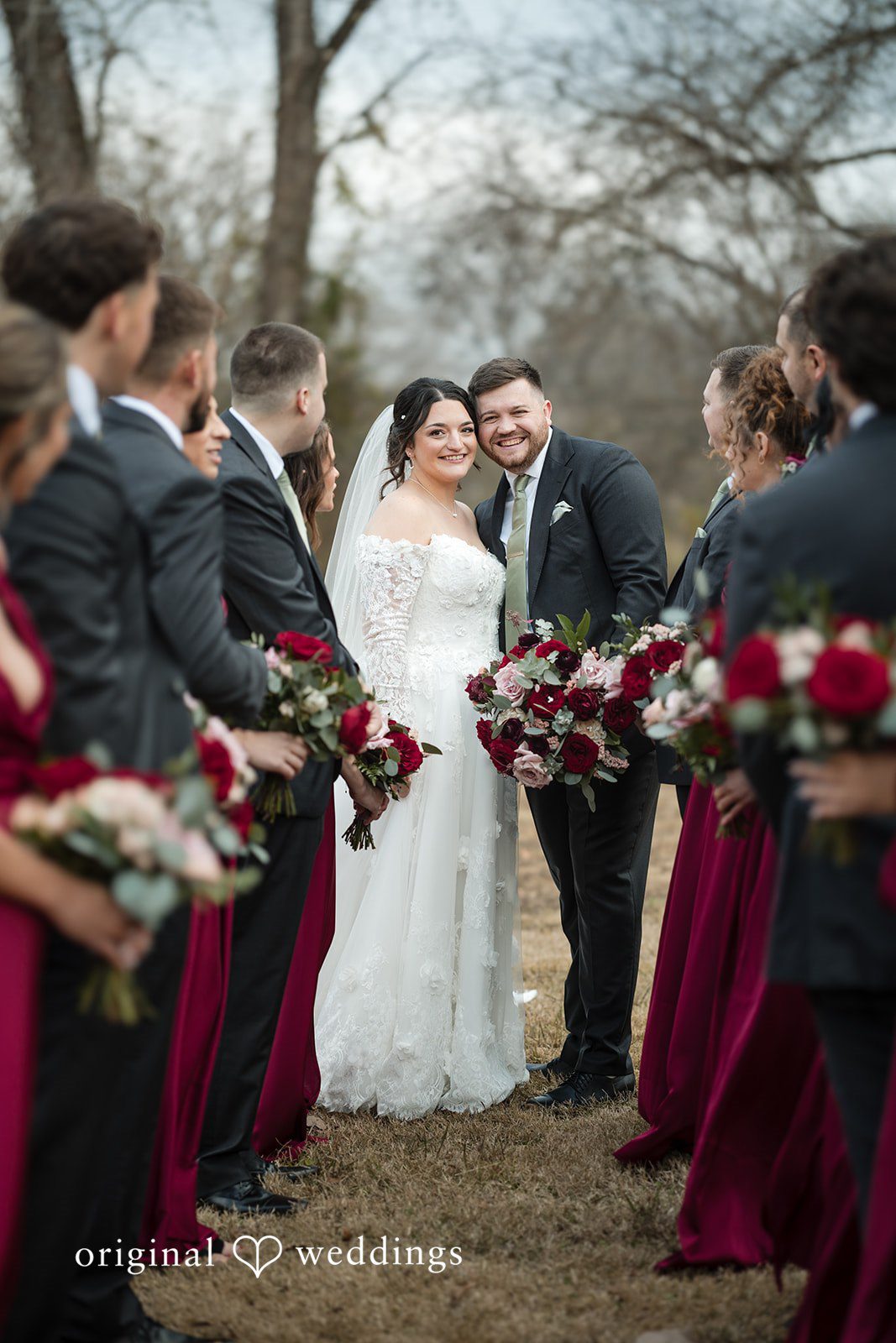 Natalie + Dakin Bride and groom walking past their wedding party holding dark red bouquets.