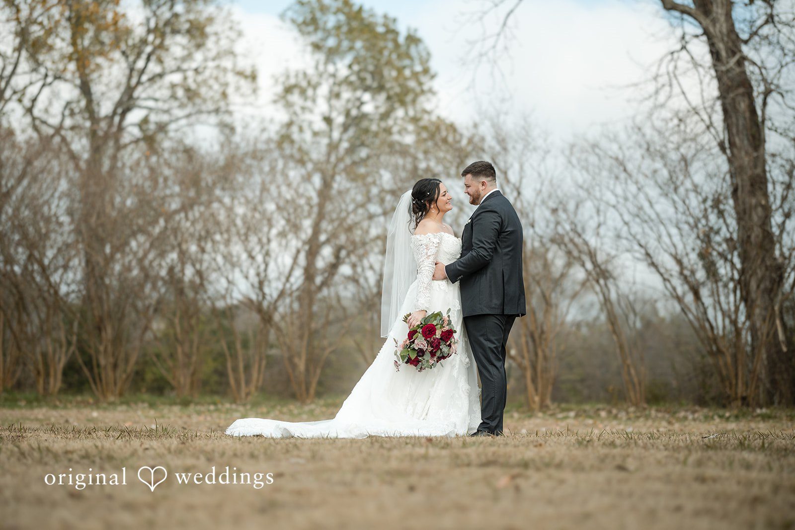 Natalie + Dakin Bride and groom embracing and looking at each other near a line of trees.