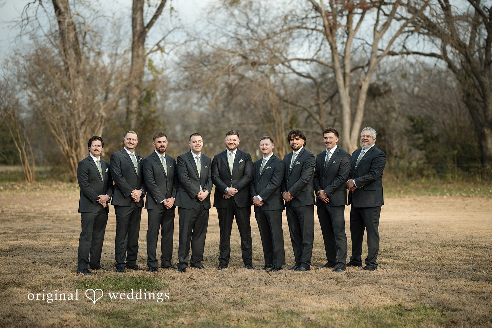 Natalie + Dakin Groom posing in a field with a lineup of groomsmen in dark suits.