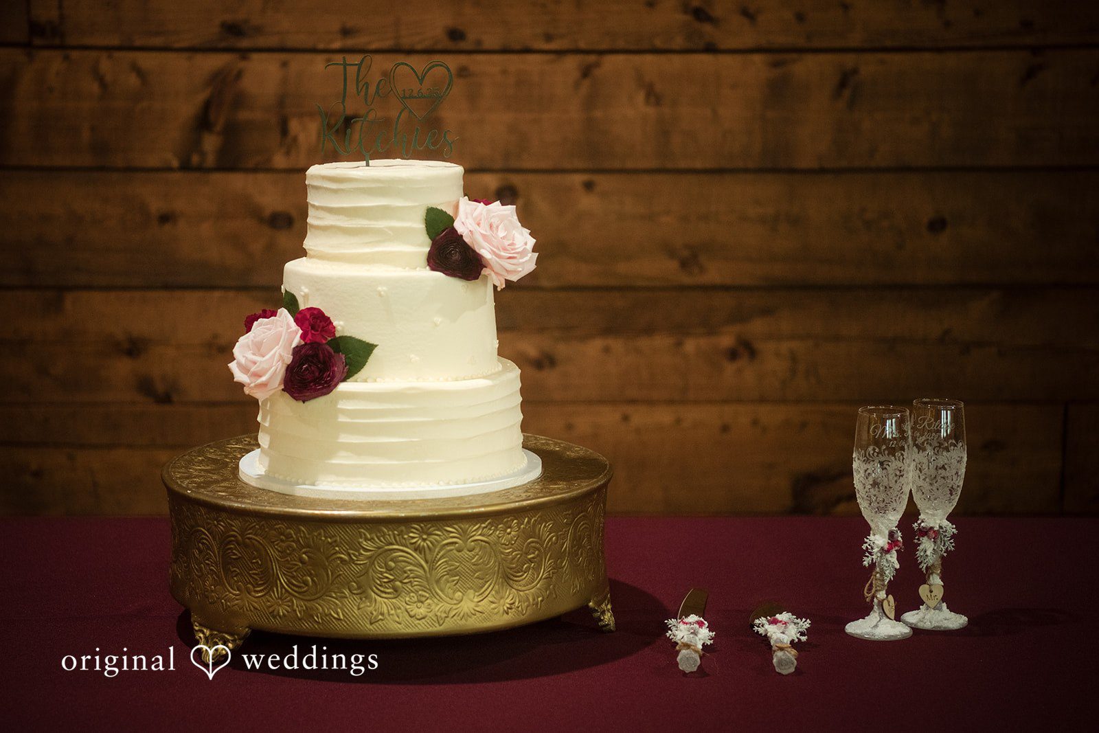 Natalie + Dakin Three-tiered smooth white wedding cake on a gold stand next to champagne flutes.
