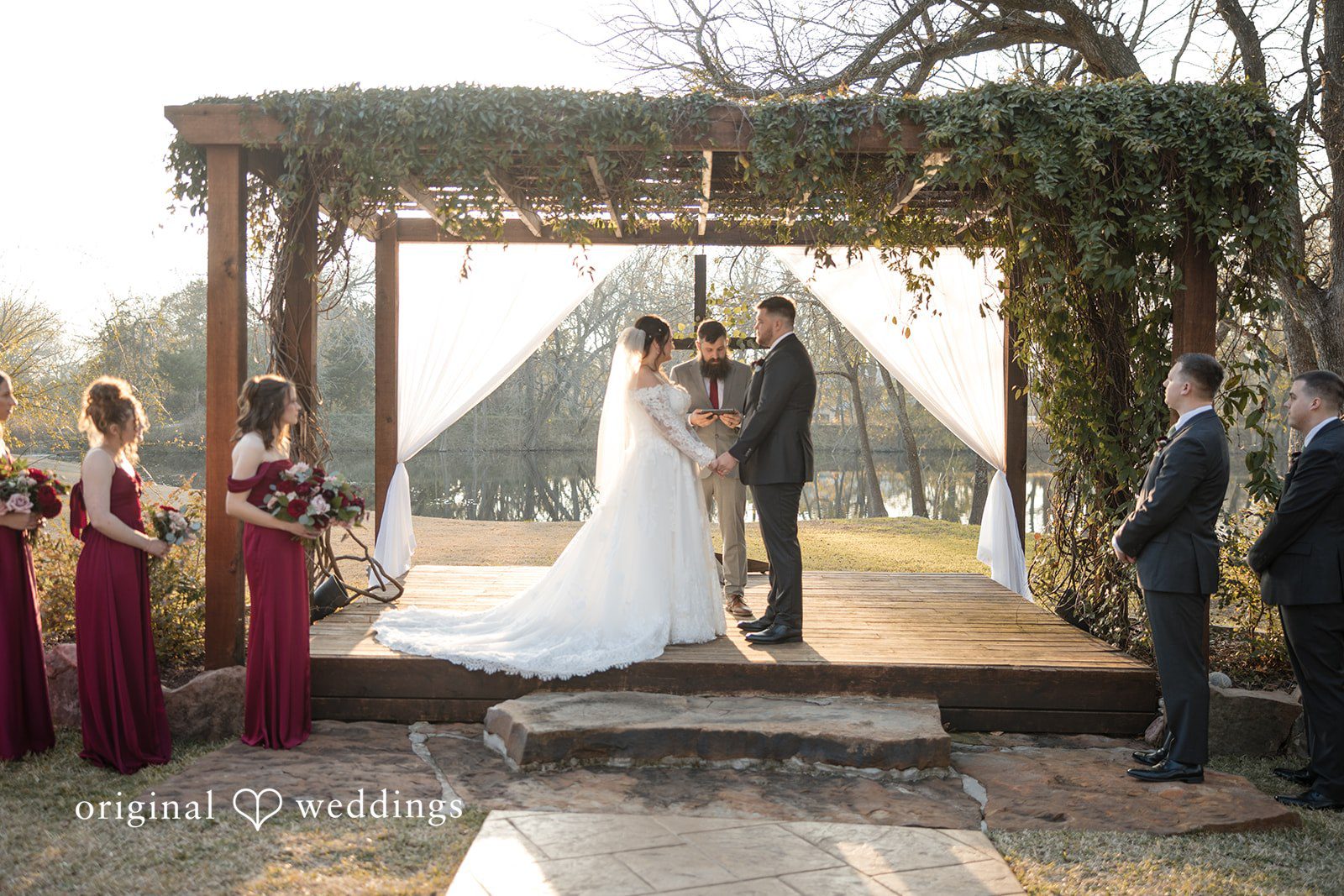 Natalie + Dakin Wide shot of a wedding ceremony under a wooden structure with draped fabric.