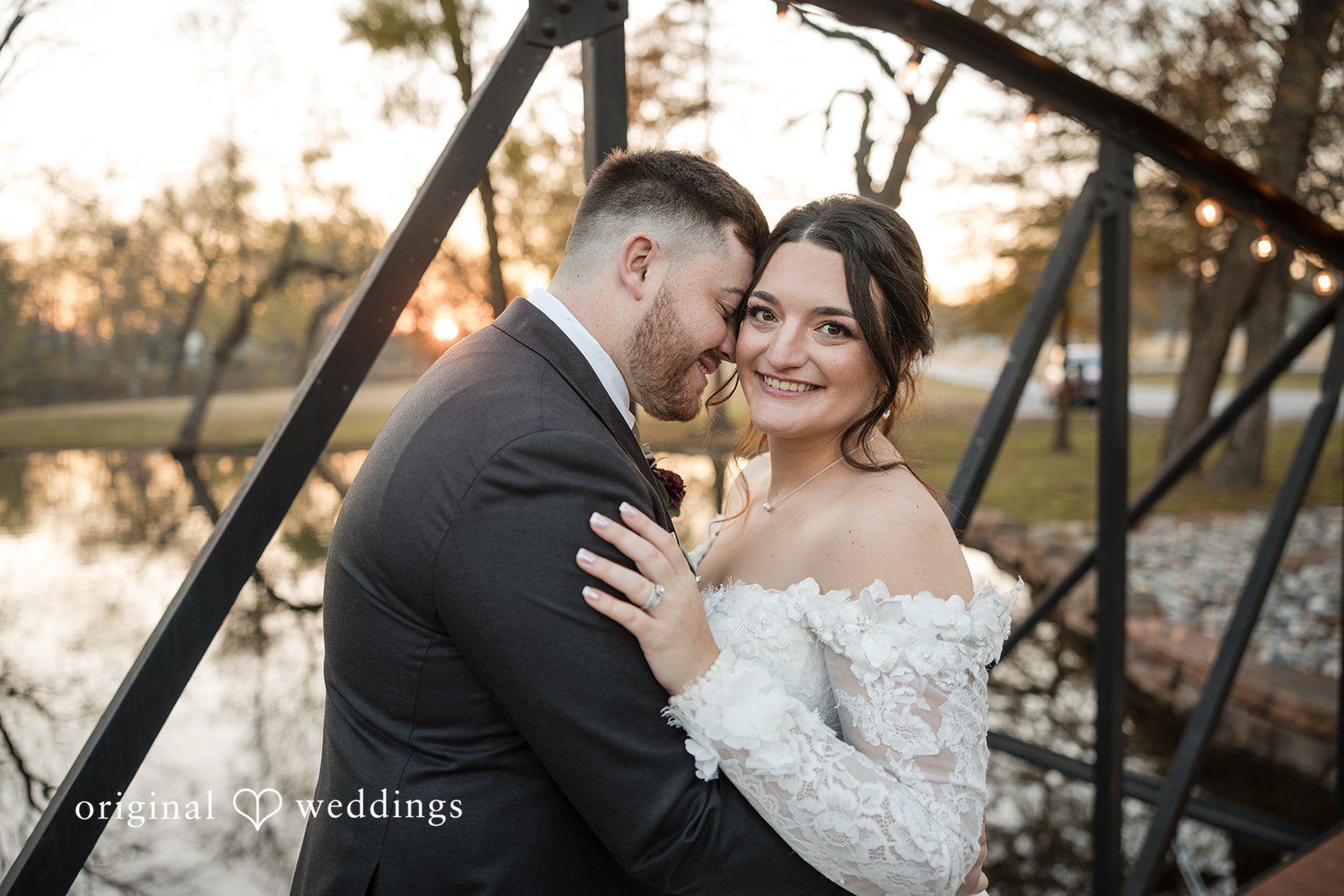 Natalie + Dakin Bride and groom smiling during a close embrace near a bridge railing.