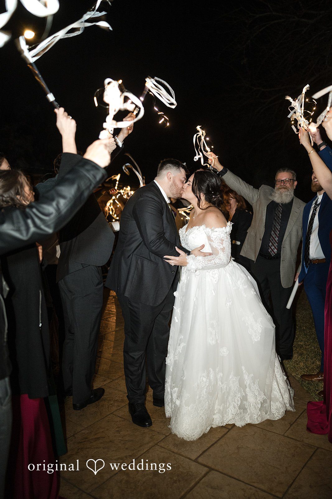 Natalie + Dakin Bride and groom kissing during a grand exit while guests wave glowing ribbon wands.