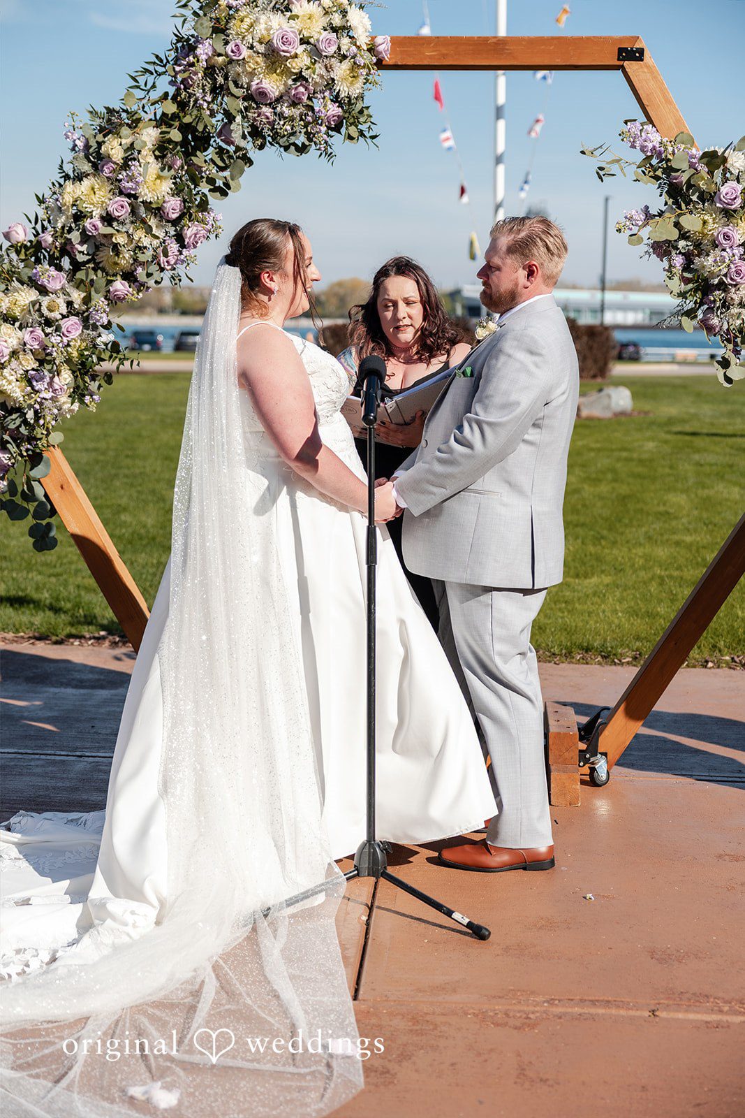 Katelyn + Bradley Bride and groom exchanging vows beneath the floral arch at DoubleTree by Hilton Port Huron captured by Detroit wedding photographers from Original Weddings.