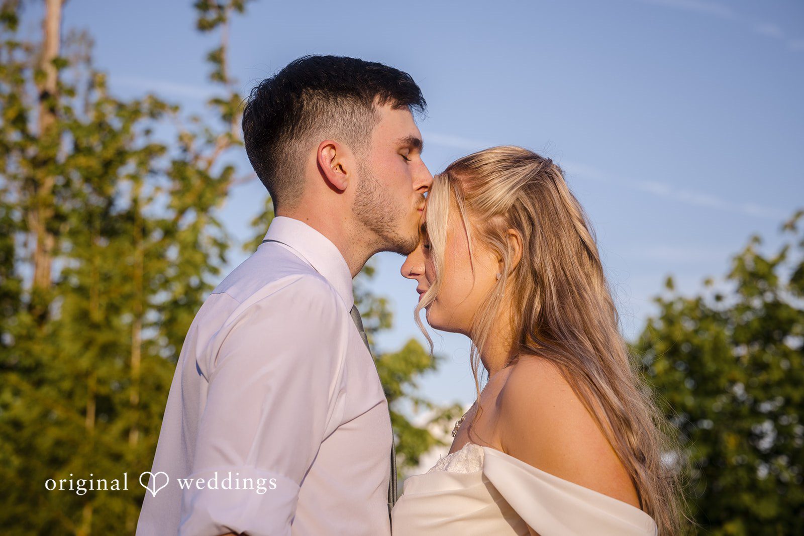 Groom kissing the bride on the forehead outdoors