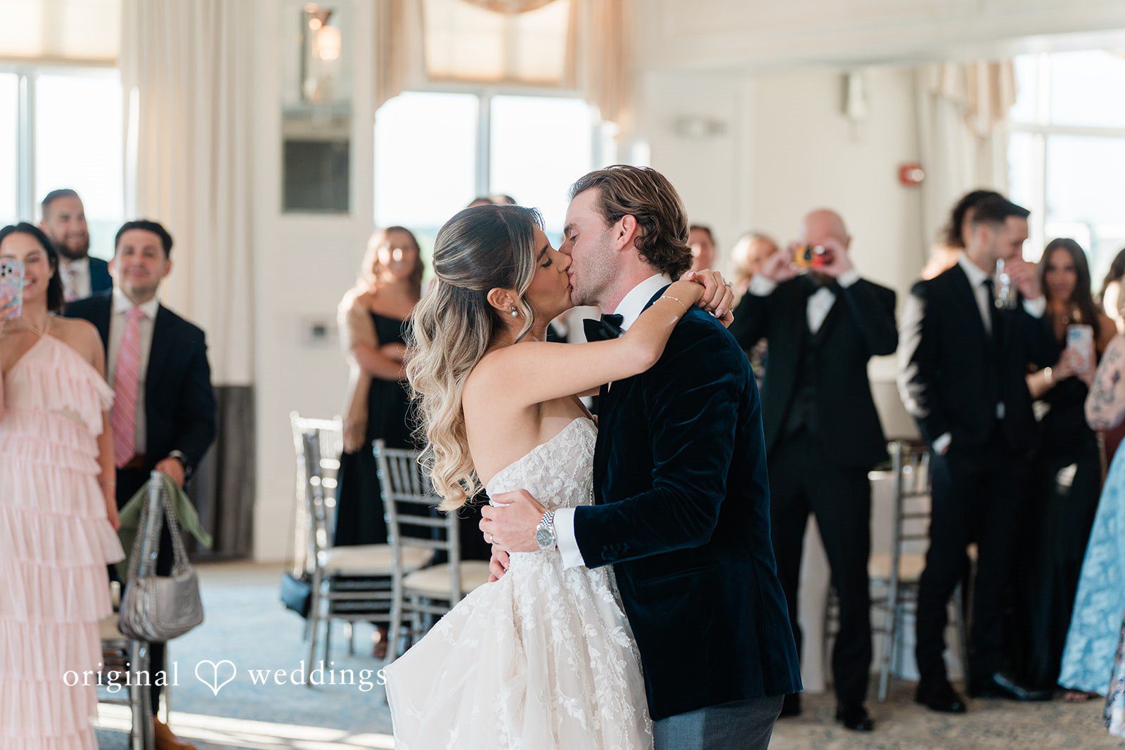 Close-up of a bride and groom embracing while dancing at their reception surrounded by guests.