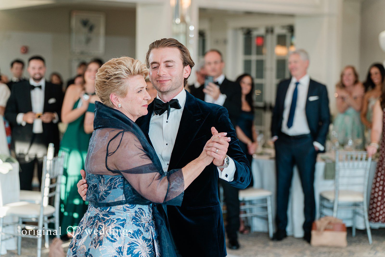 room sharing a dance with a woman in a patterned blue dress during a wedding reception.