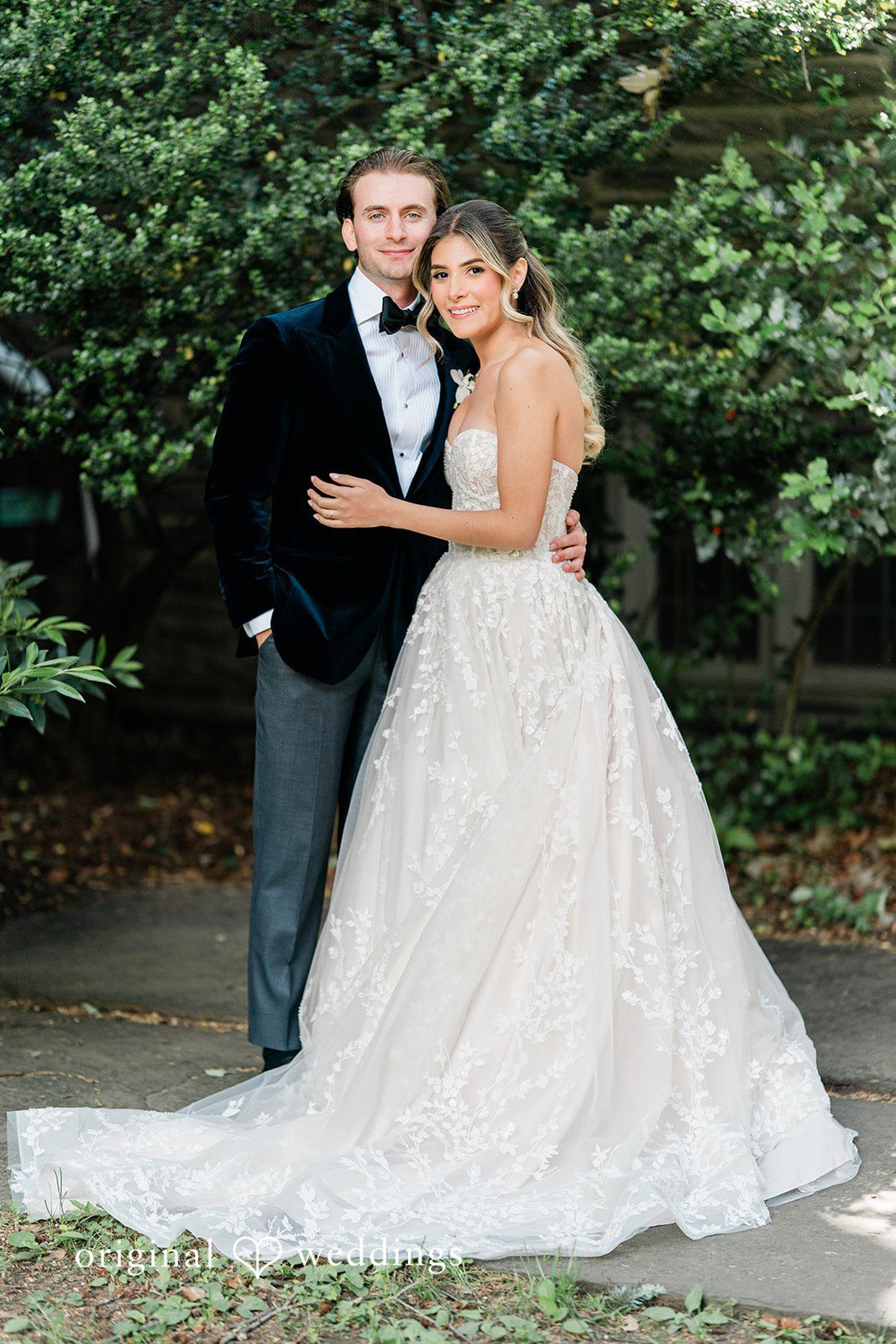 Bride and groom embracing and smiling together against a background of green foliage.