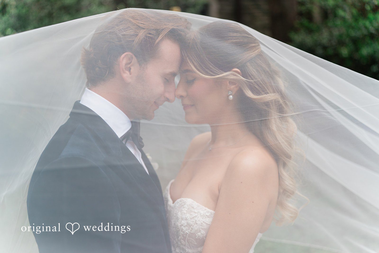 Close-up profile view of a bride and groom leaning close together under a sheer bridal veil.