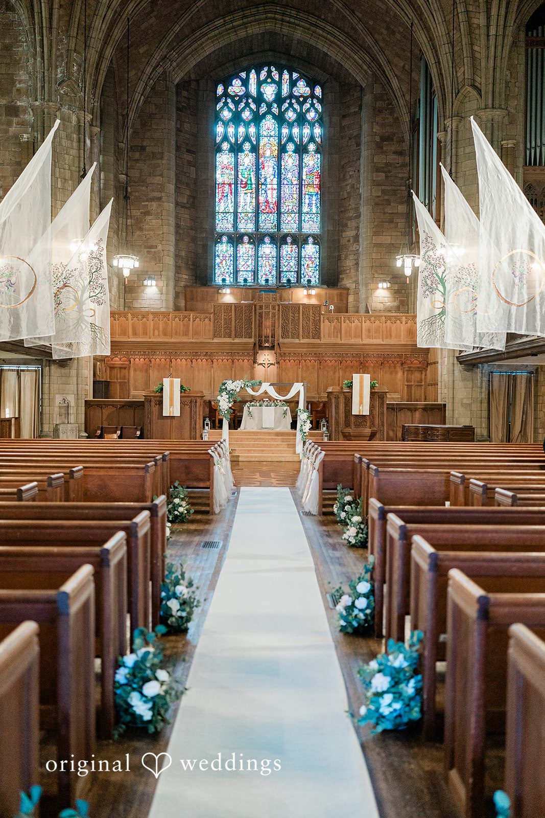 Church sanctuary aisle lined with wooden pews leading toward a grand stained-glass window.