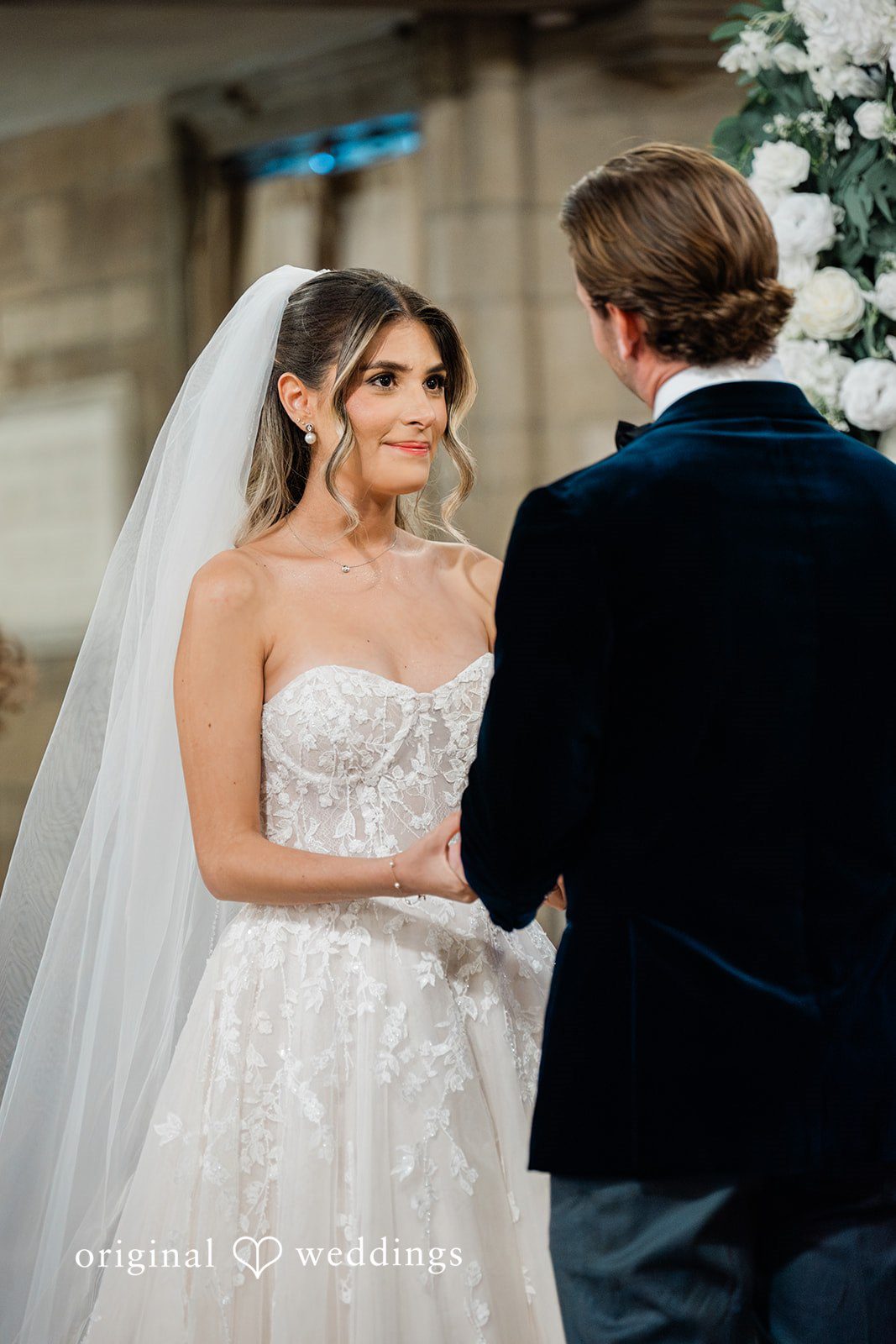 Bride looking lovingly at the groom while holding hands at the altar.
