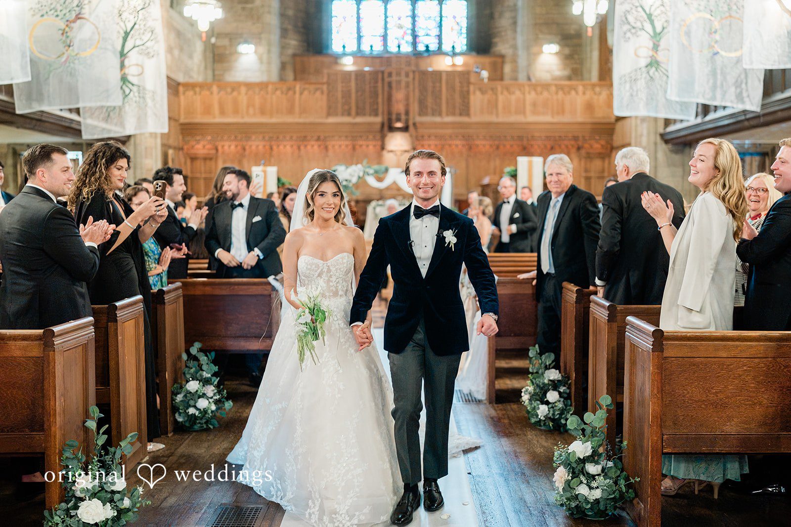 Bride and groom walking down the aisle together while wedding guests applaud.