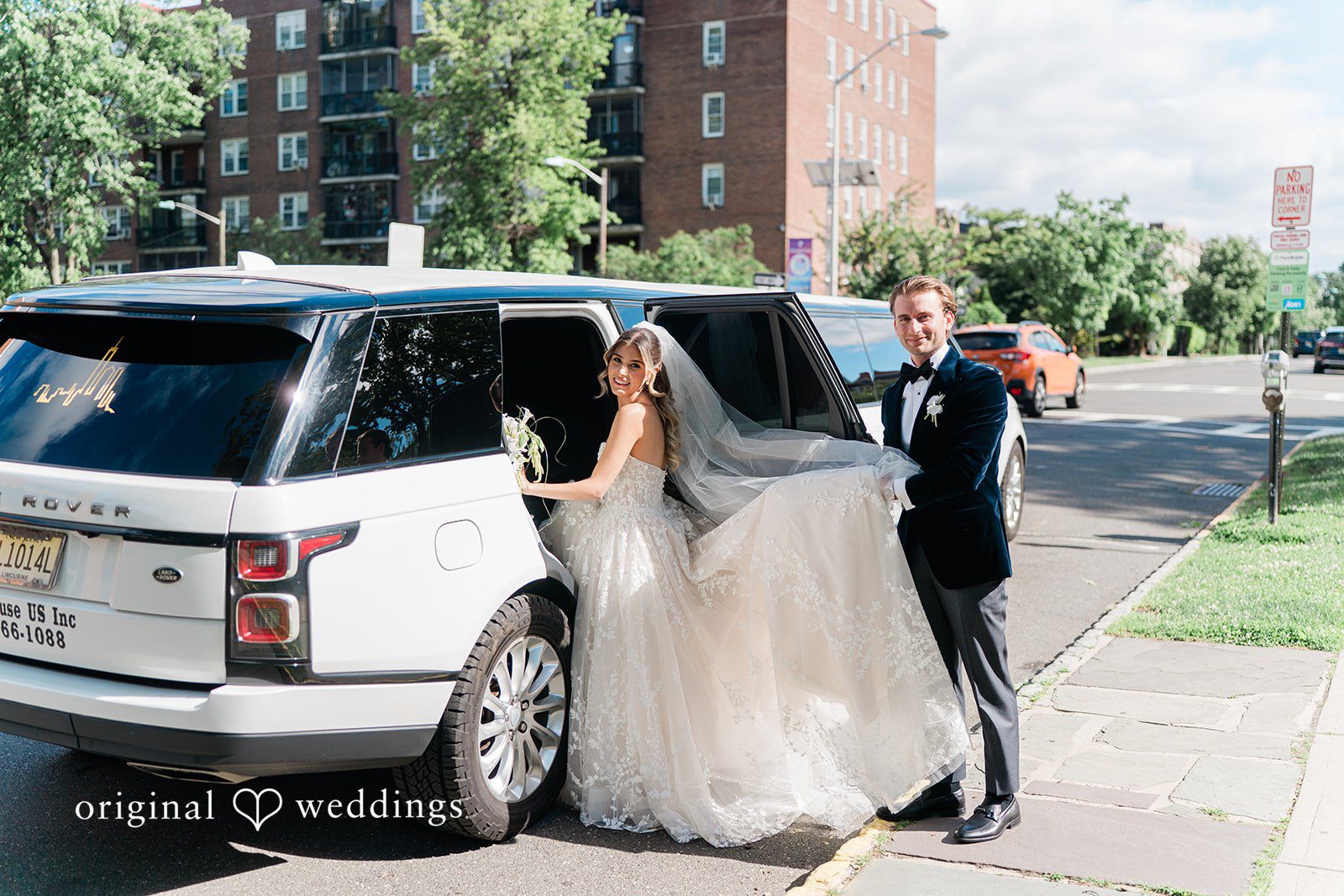 Groom holding the door open for his bride as she steps into a white luxury SUV.