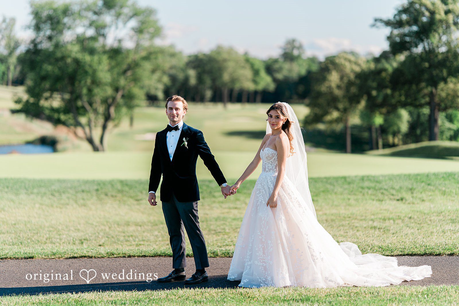 Bride and groom holding hands while walking across a vast green lawn.