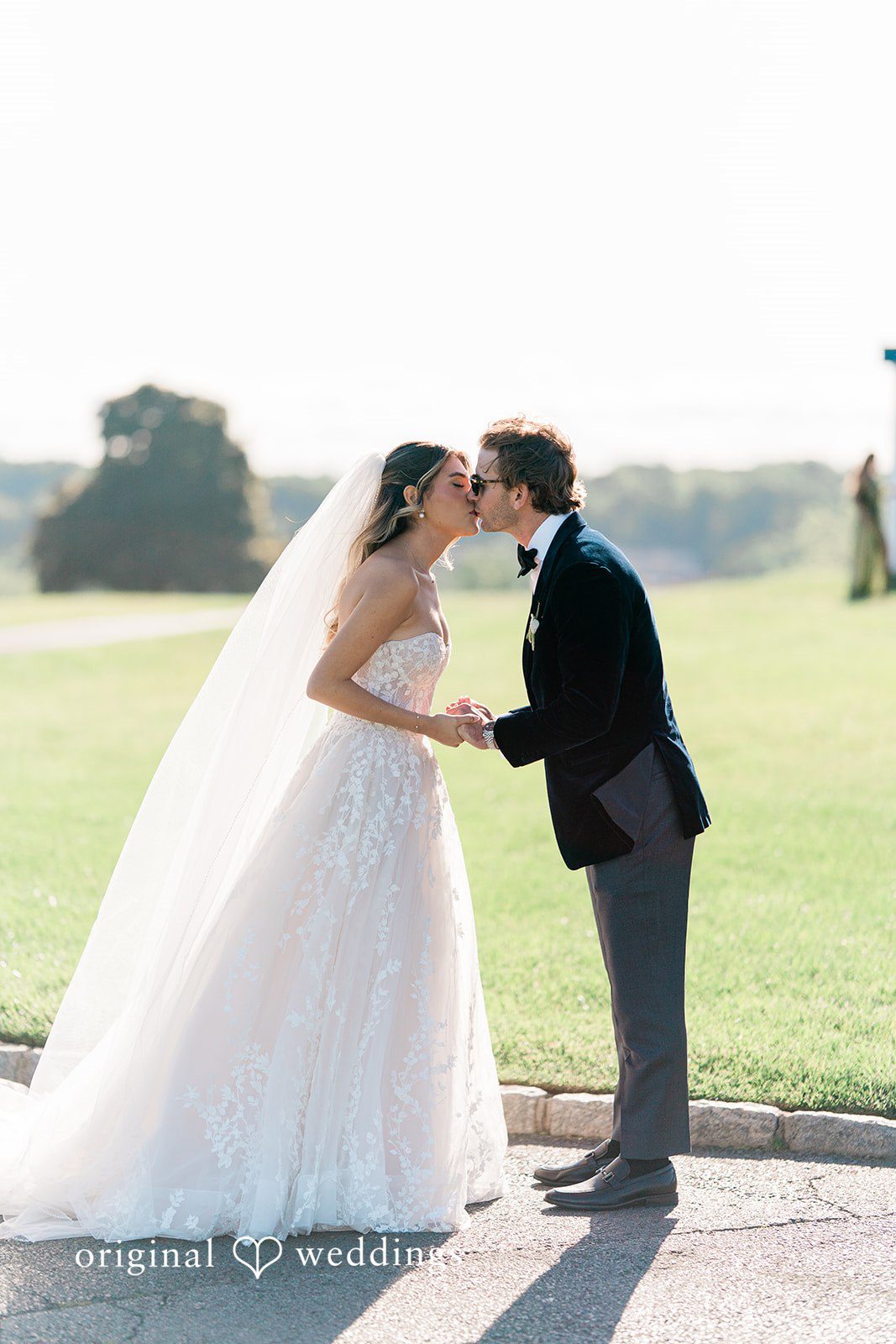 Bride and groom sharing a kiss on a stone pathway with a grassy field in the background.