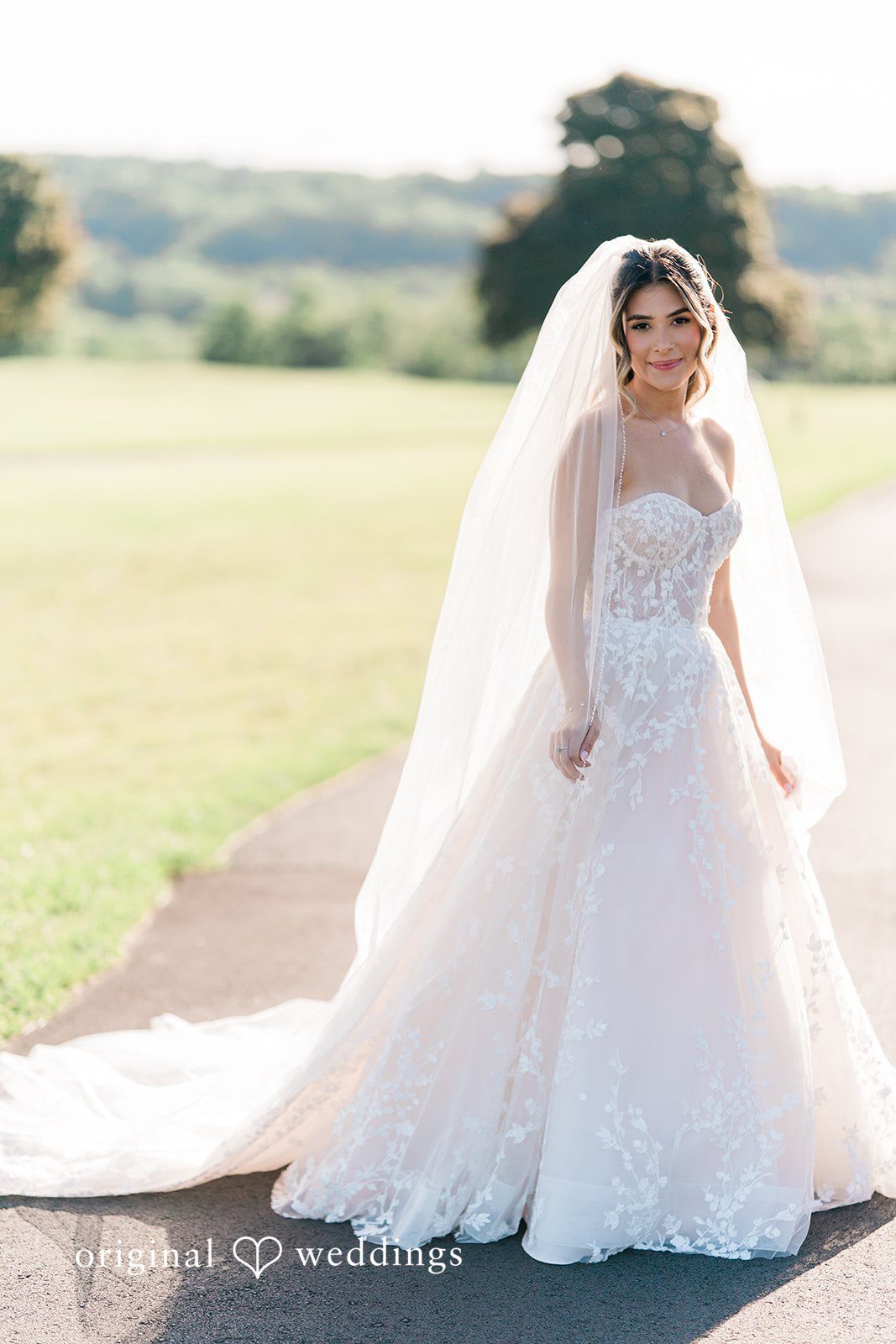 Bride in a full white ballgown and long veil standing on a paved pathway.