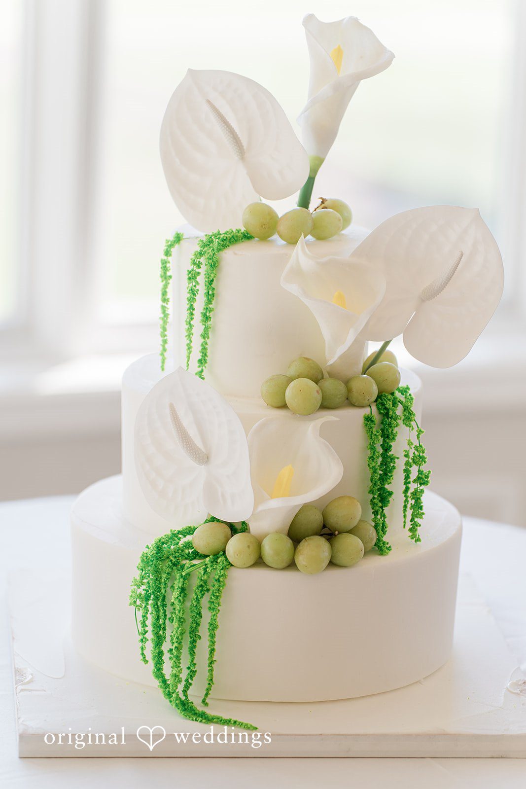 Three-tiered white wedding cake decorated with green grapes and white calla lilies.