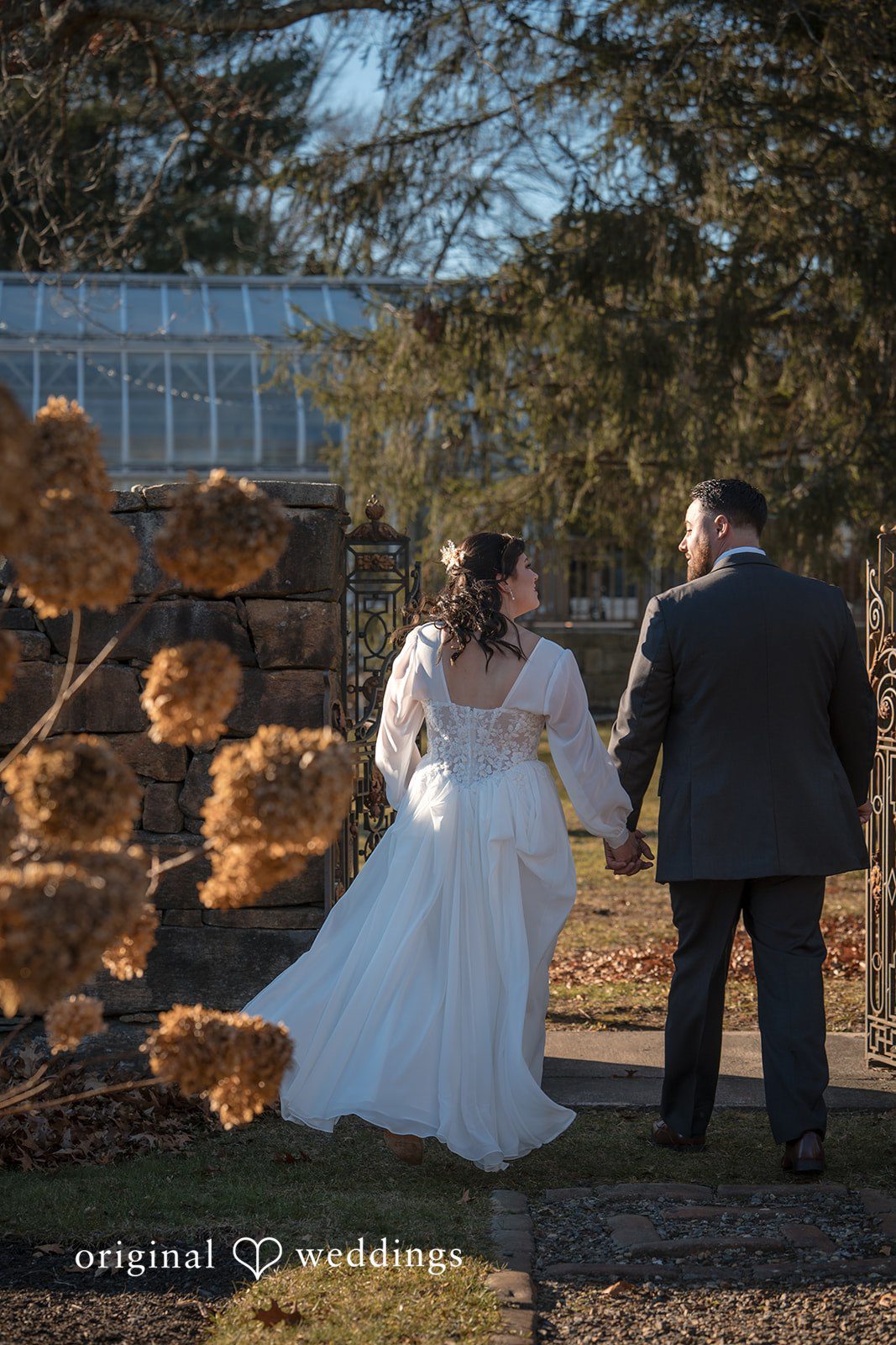 Carolyn + Robert Newlywed couple walking hand in hand in an outdoor setting.