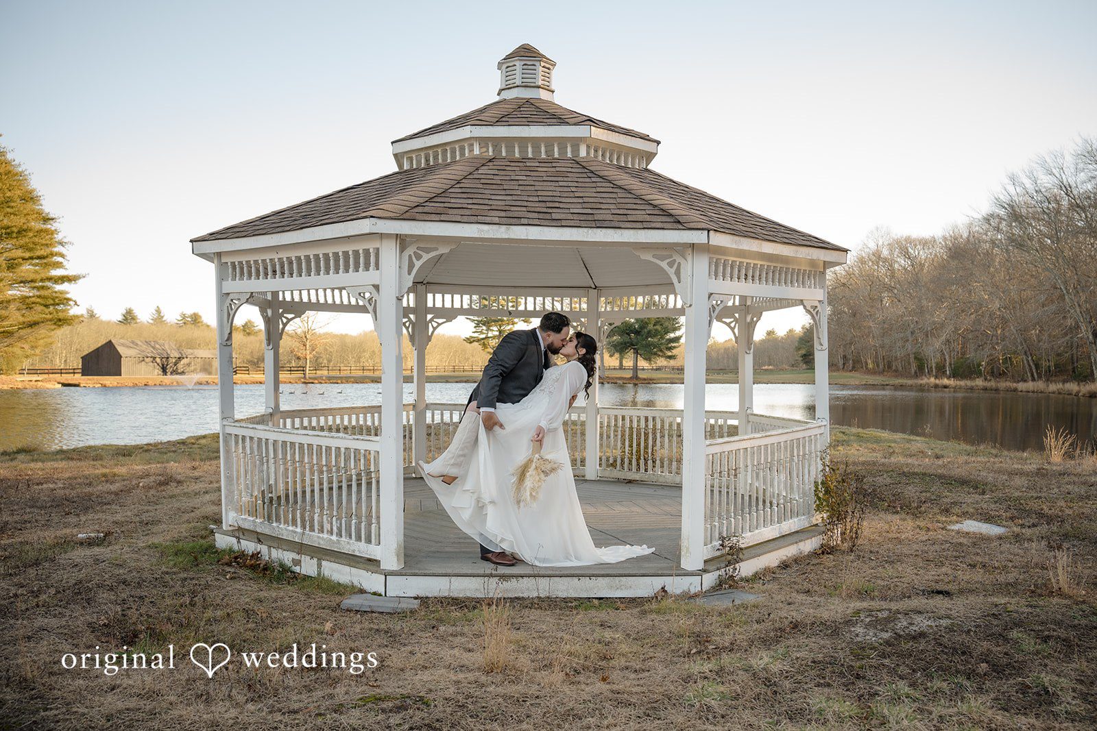 Carolyn + Robert Newlywed couple standing together inside a white gazebo by the water.