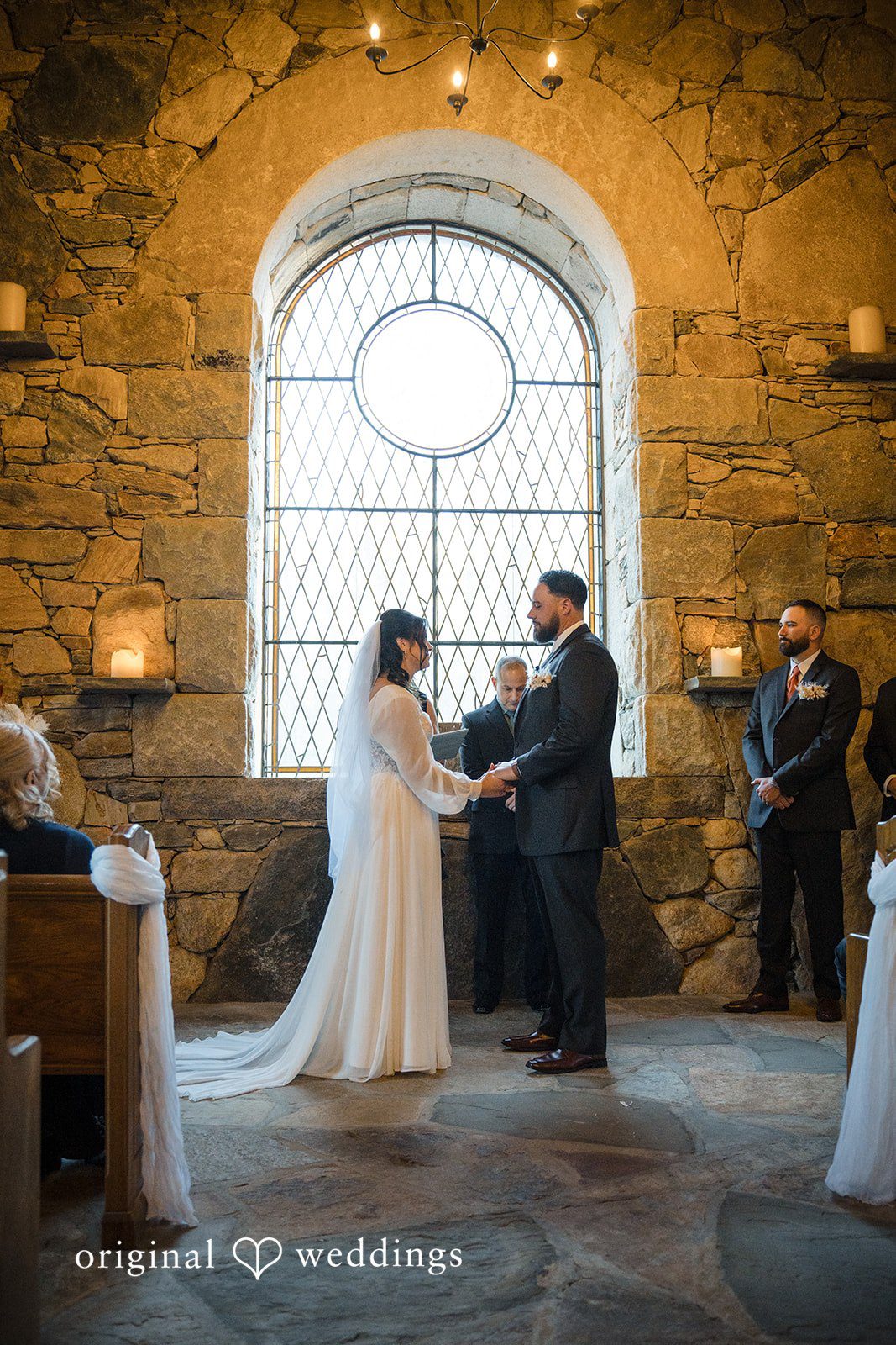 Carolyn + Robert Bride and groom exchanging vows inside a stone church during their wedding ceremony.