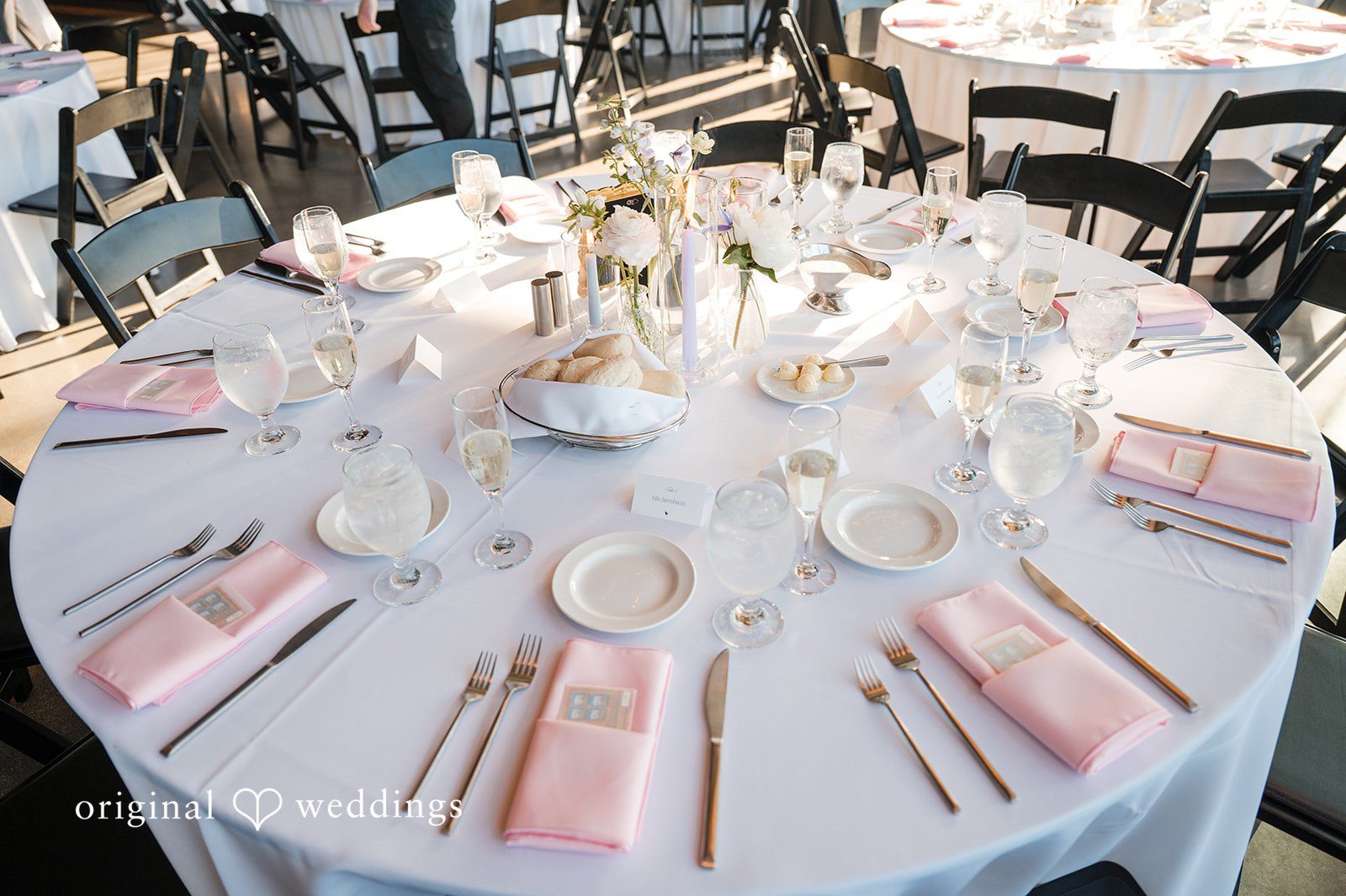 Elegant reception table setting with pink napkins, bread basket, and floral centerpiece