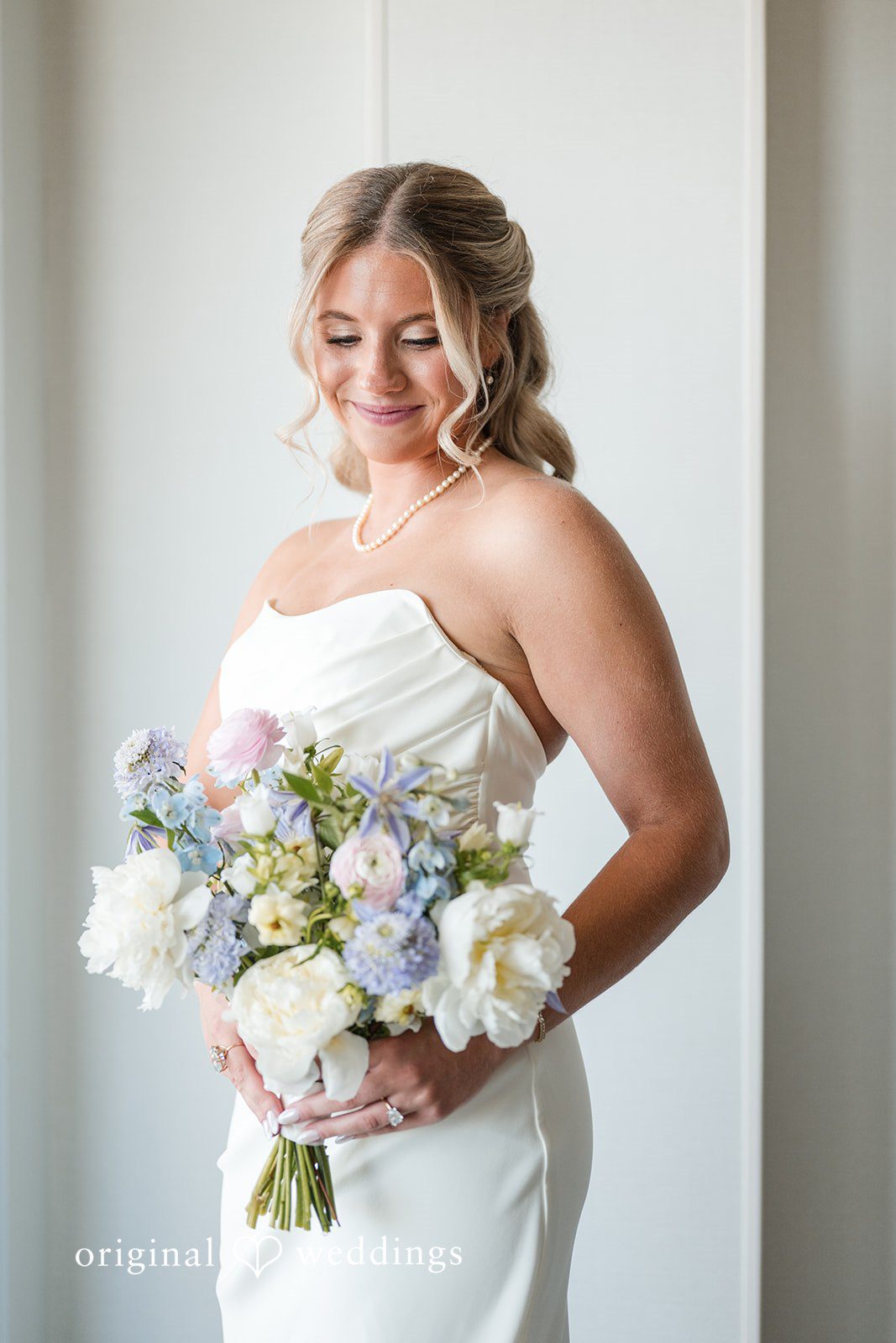 Bride holding pastel bouquet in elegant bridal portrait with pearl necklace and soft window light