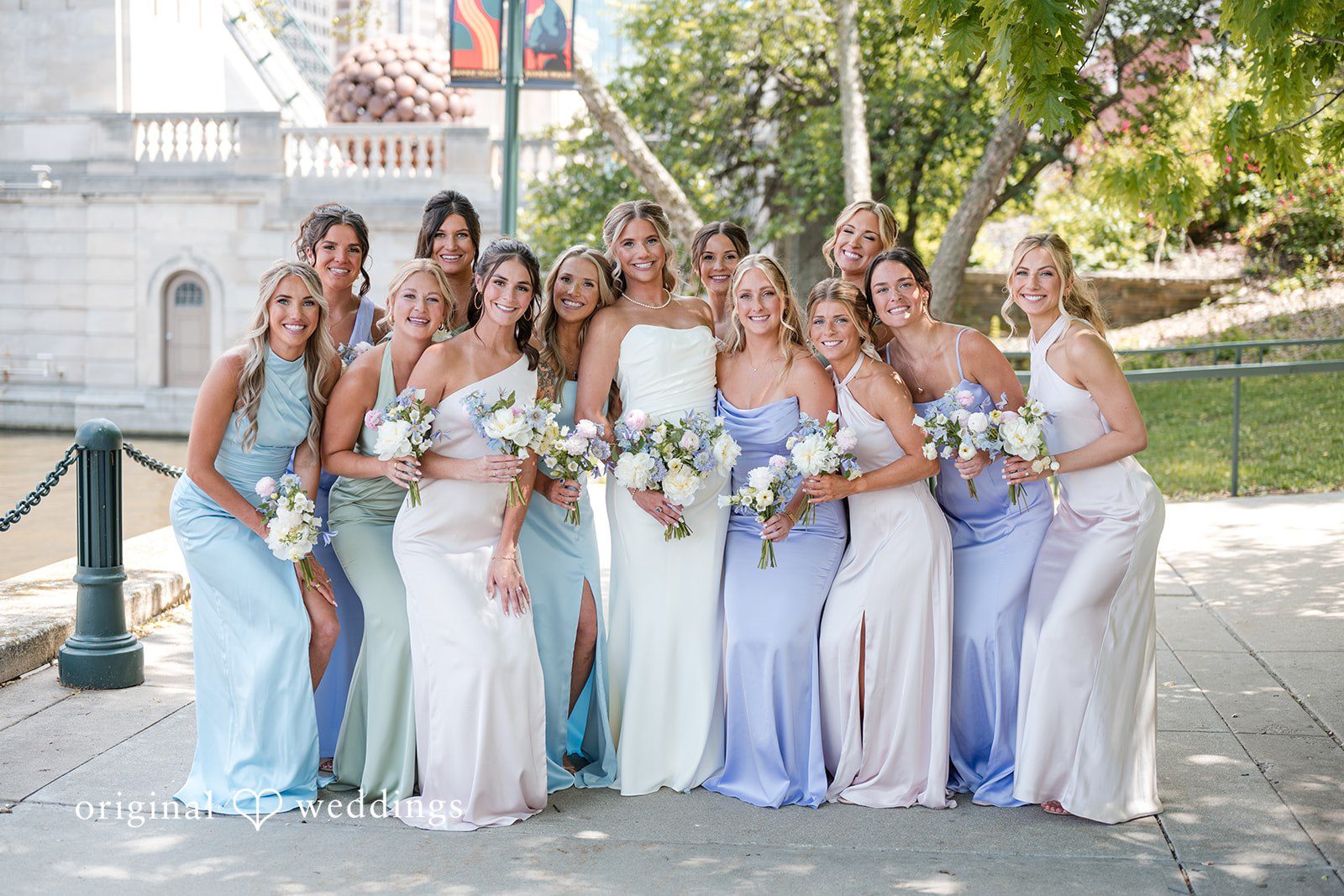 Bride posing with bridesmaids in pastel dresses holding matching bouquets outdoors