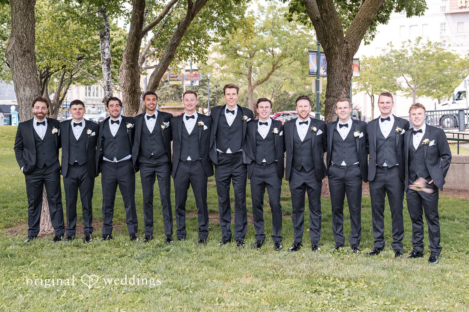 Groom posing with groomsmen in matching black tuxedos for wedding party portrait