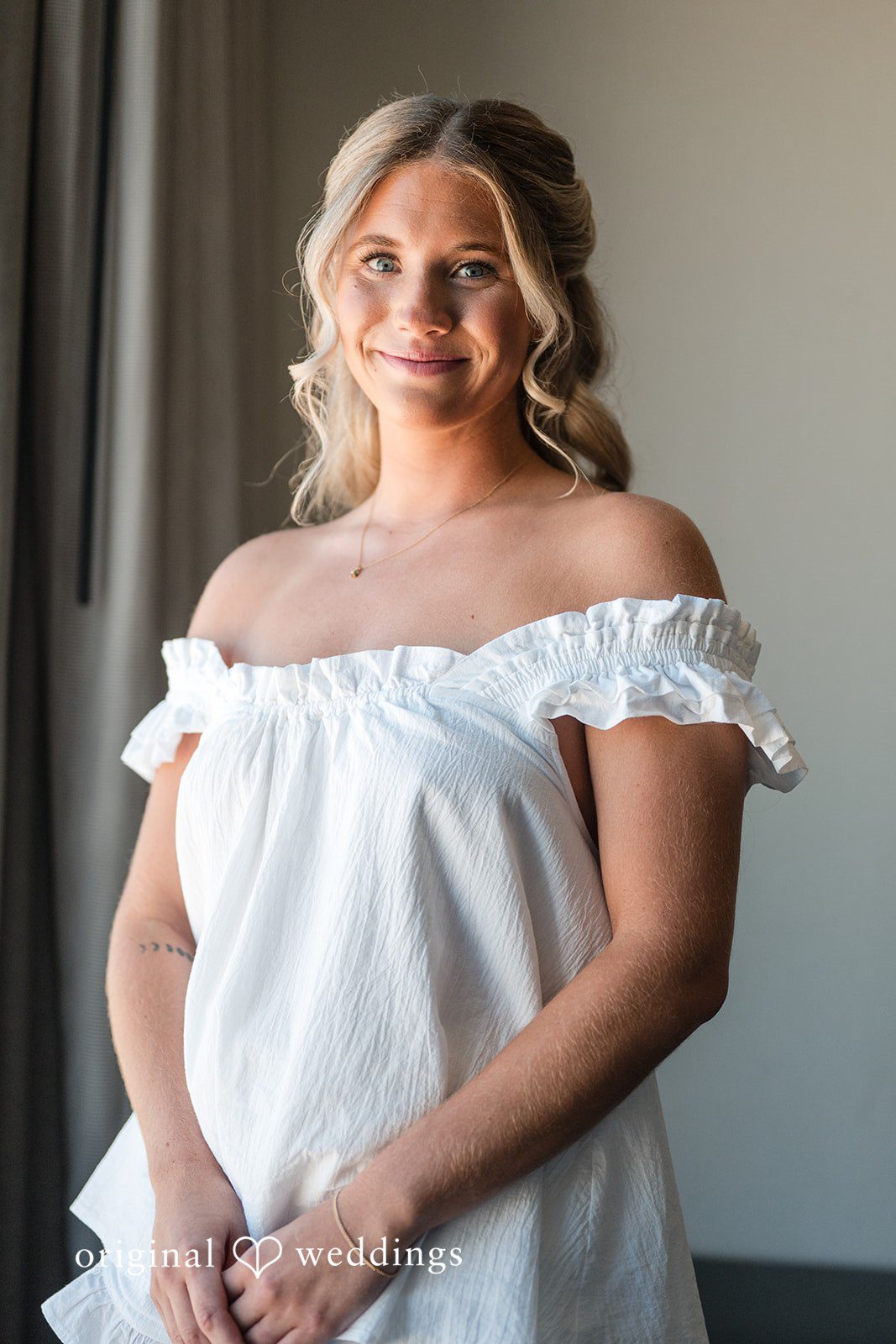 Bride in white getting-ready dress posing by window with soft natural light