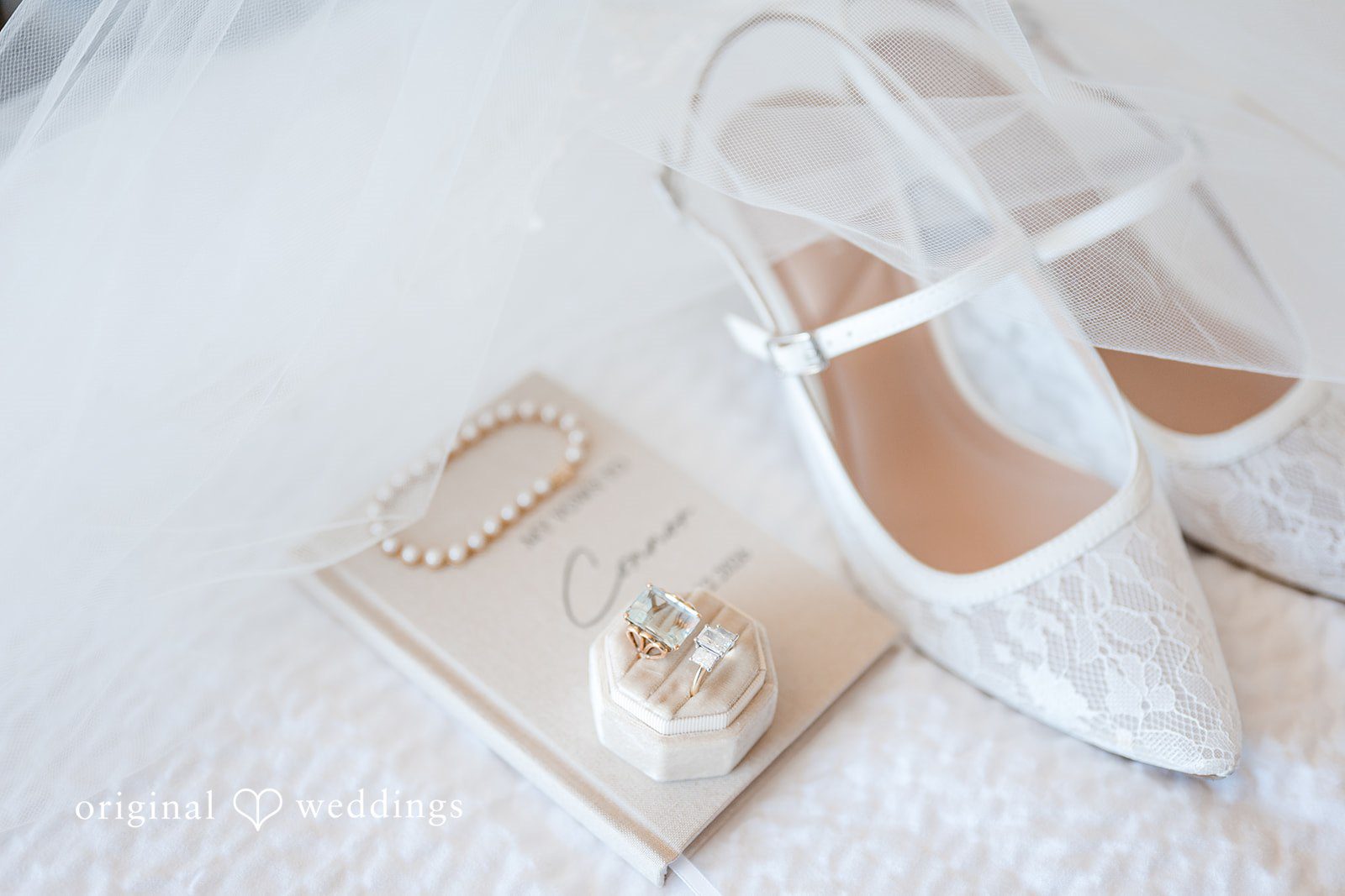 Bridal accessories including lace shoes, wedding rings, pearls, and veil arranged for detail shot