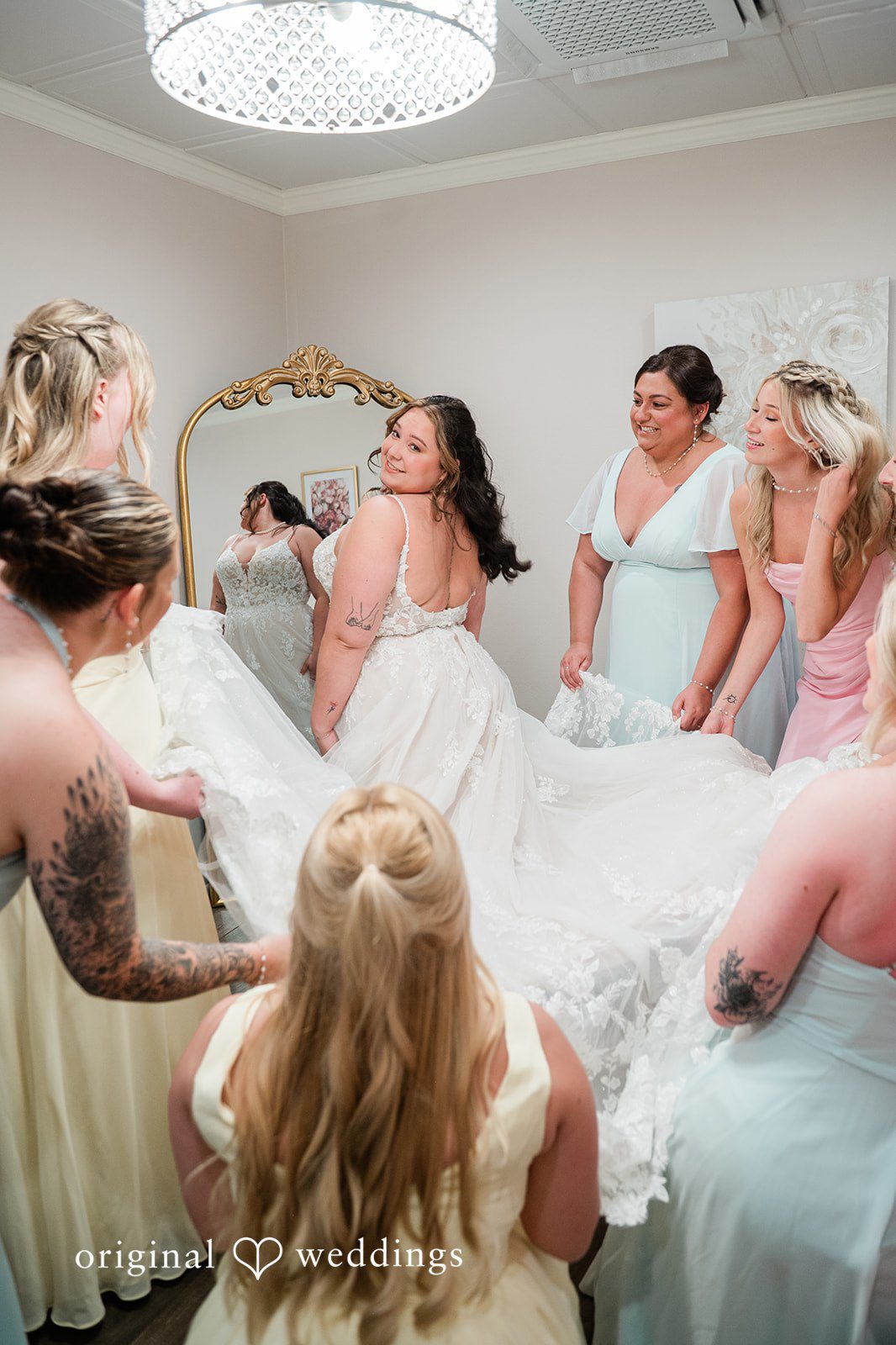 Janissa + Josh Beautiful picture of bride with the bridesmaids holding the bride's gown