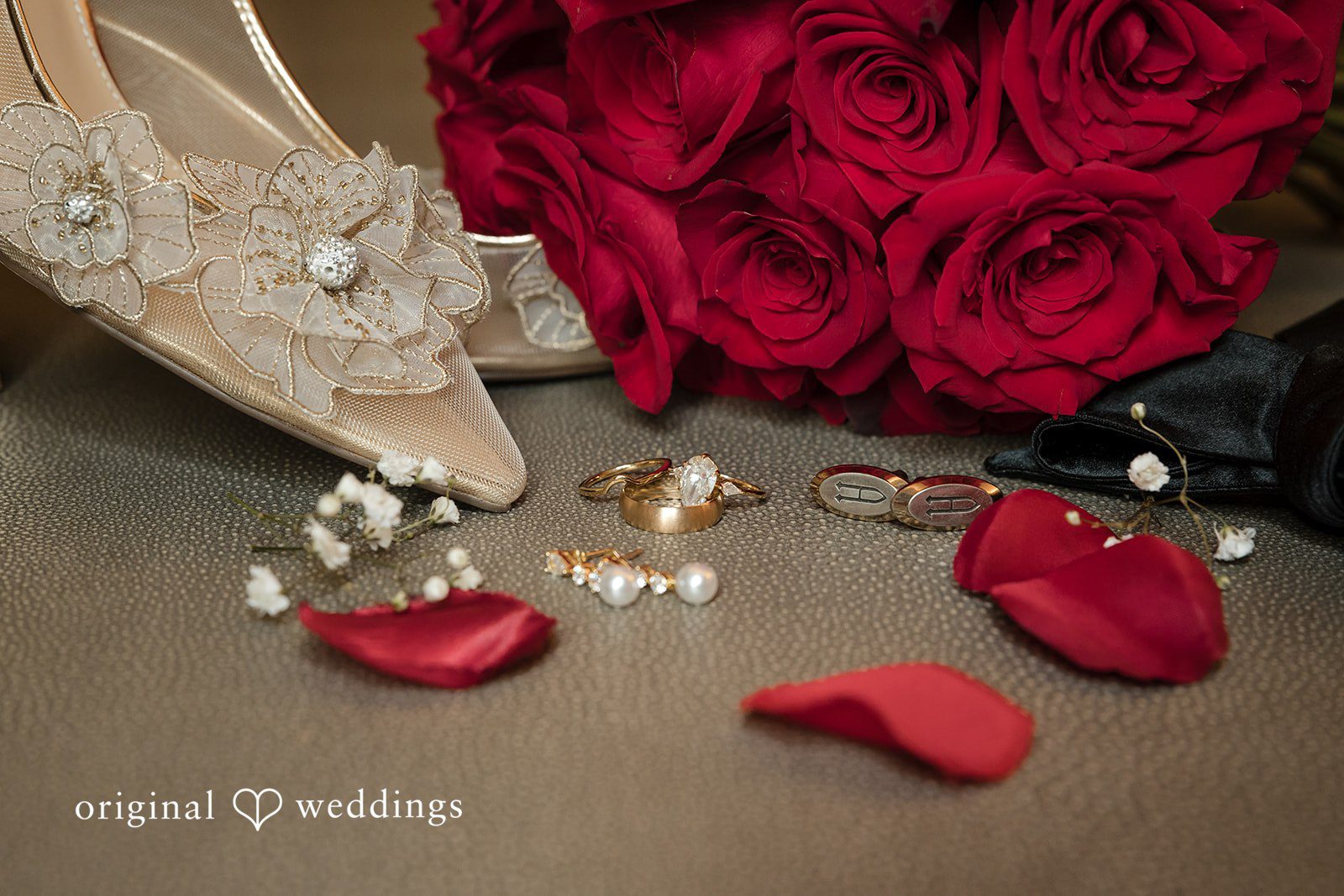 Detailed shot of wedding rings, jewelry, and red rose petals on a surface.