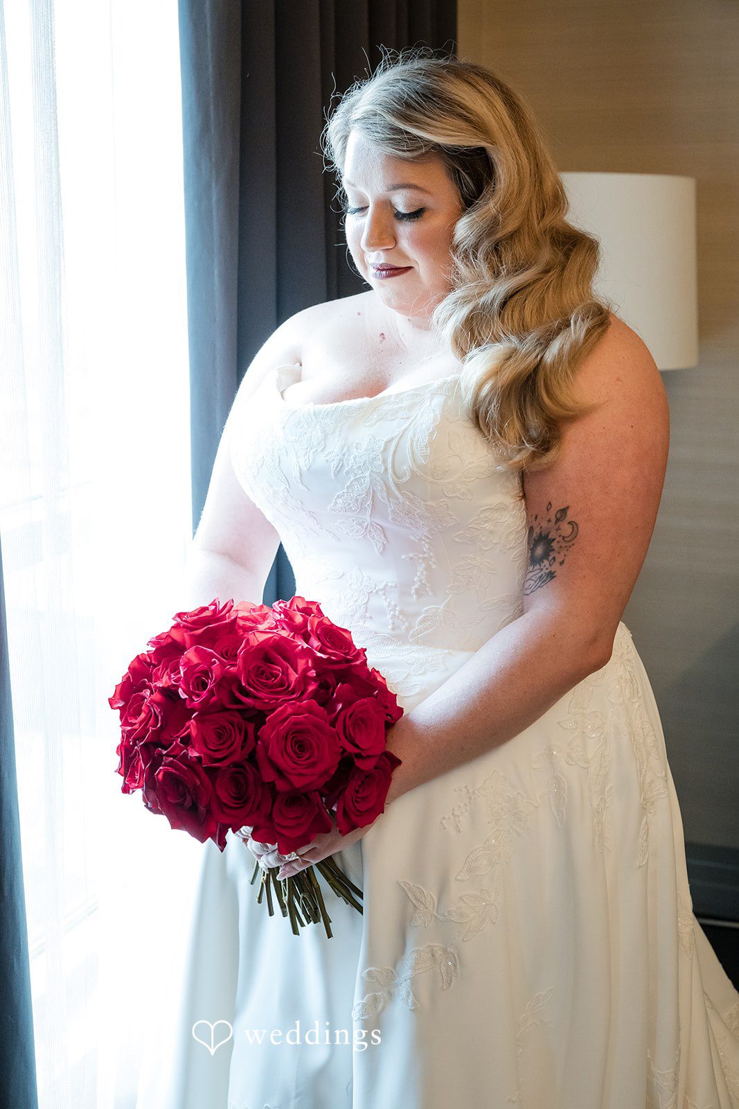 Bride in a white gown holding a large bouquet of red roses.
