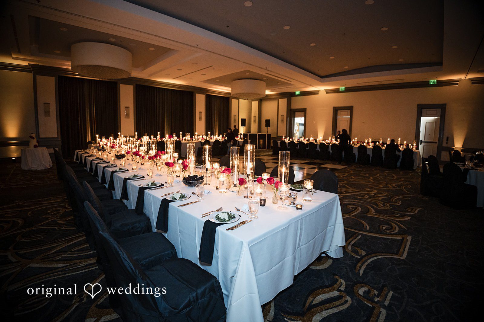 Long banquet table with white tablecloth, black runner, and numerous glowing candles.