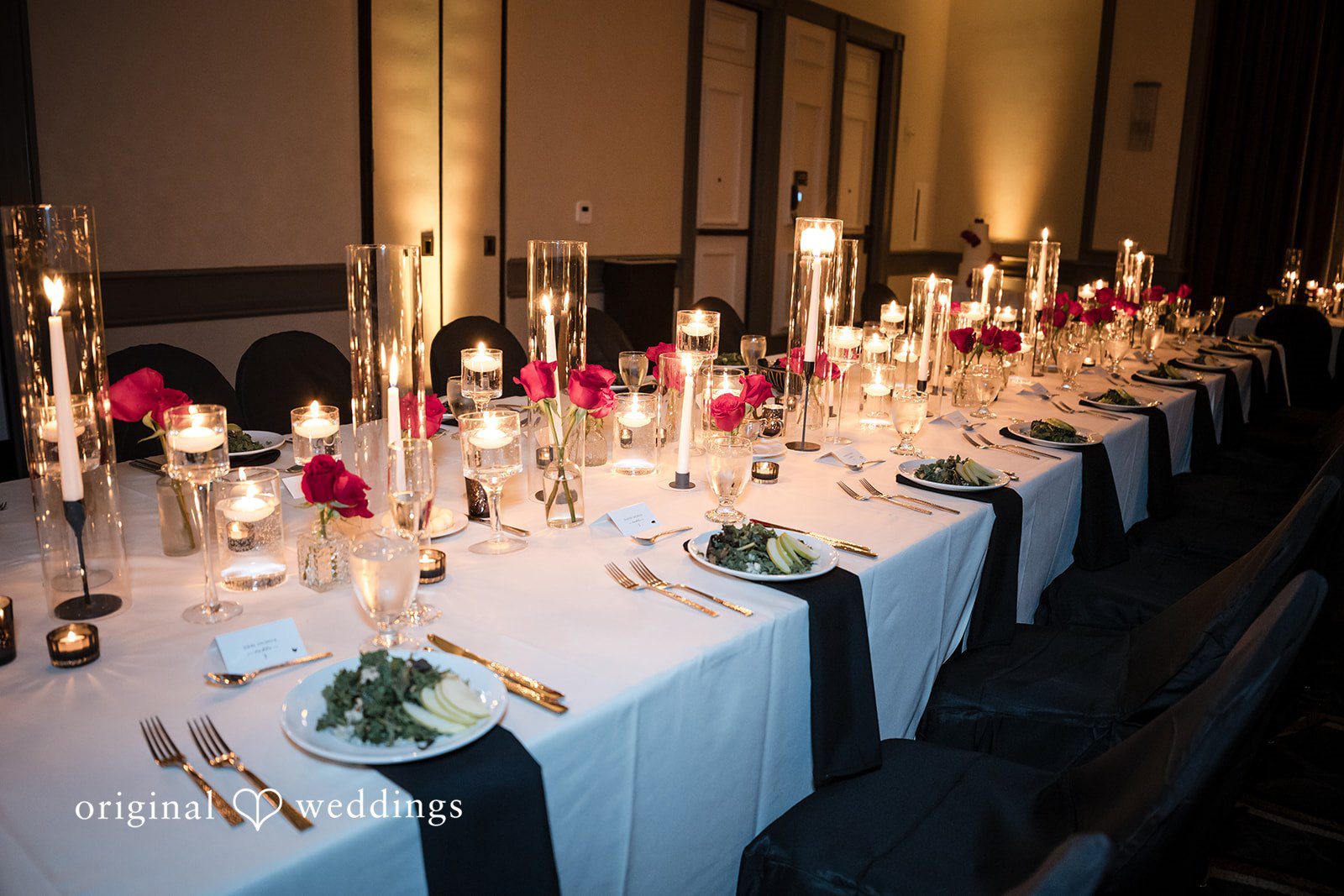 Close-up of a decorated long table featuring tall glass candle holders and greenery at Hilton Dallas.