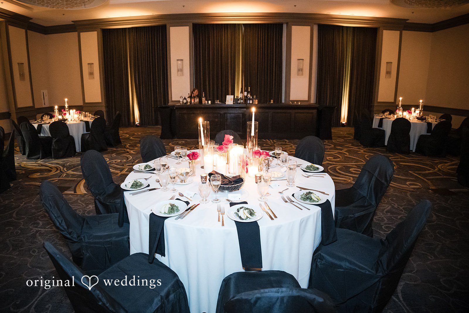 Round reception table set with white linens, black chairs, and a candle centerpiece.