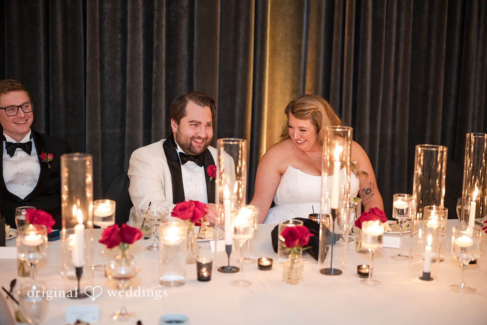 Bride and groom sitting together at a candlelit head table during the reception.