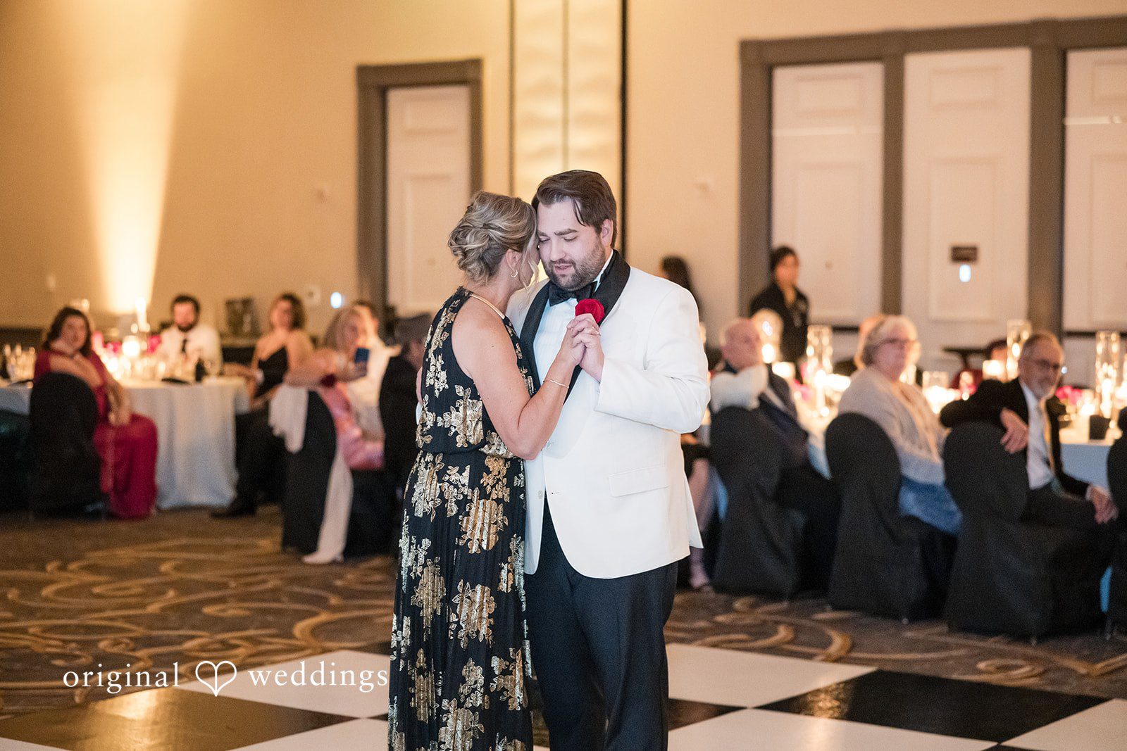 Groom dancing with a woman in a dark patterned dress on the dance floor.