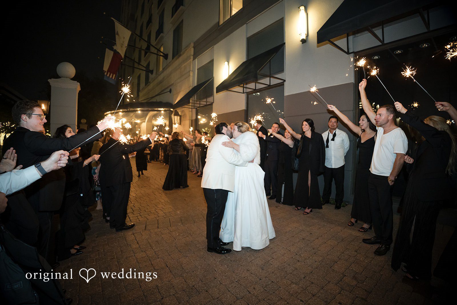 Close shot of the bride and groom kissing in the center of a sparkler exit line.