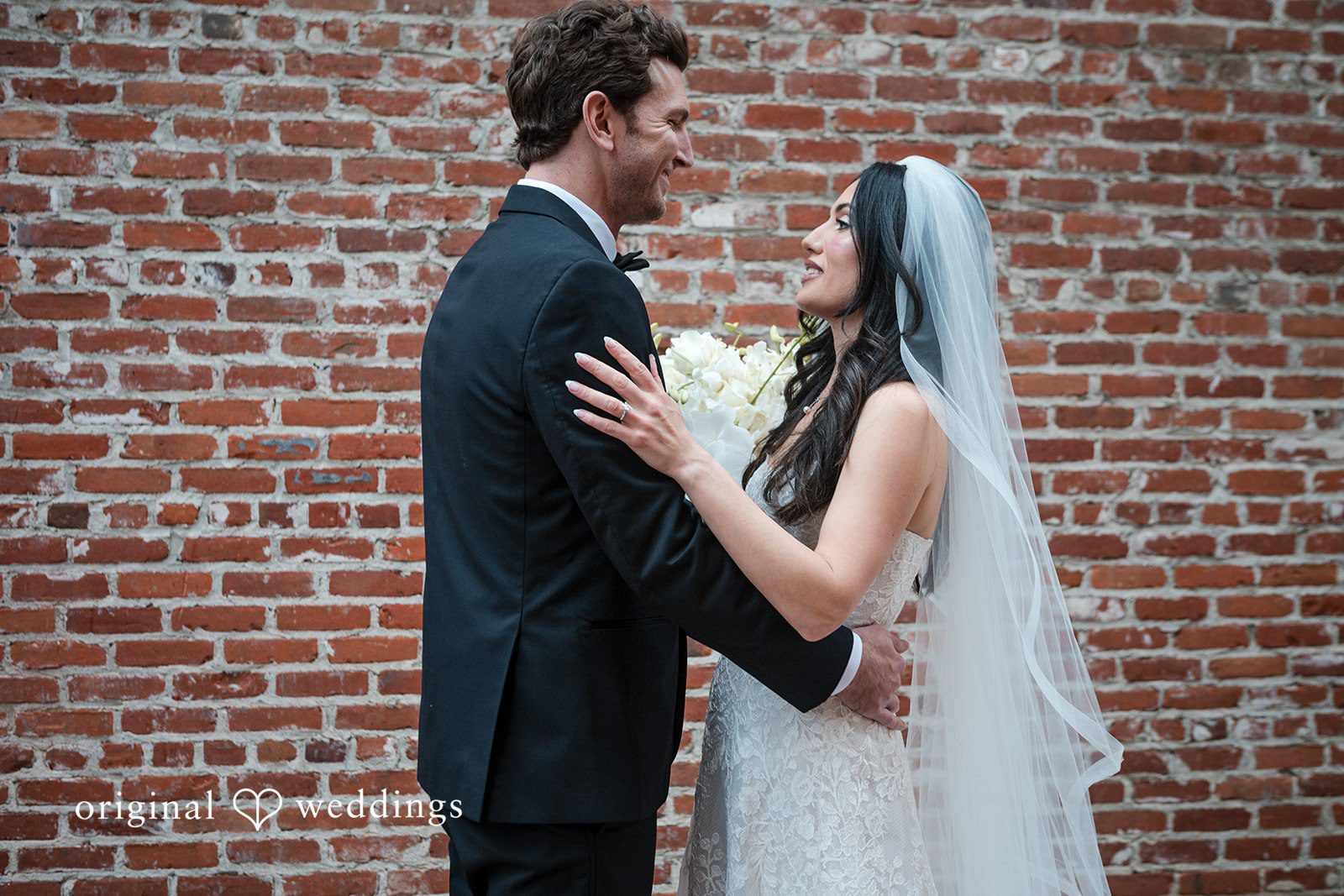 Tabatha + Justin A bride and groom face each other closely while posing near a brick wall.