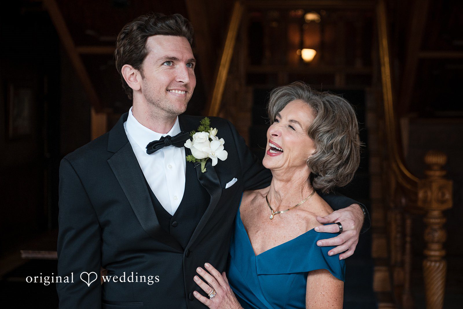 Tabatha + Justin A smiling groom in a black tuxedo embraces a woman wearing a blue dress.