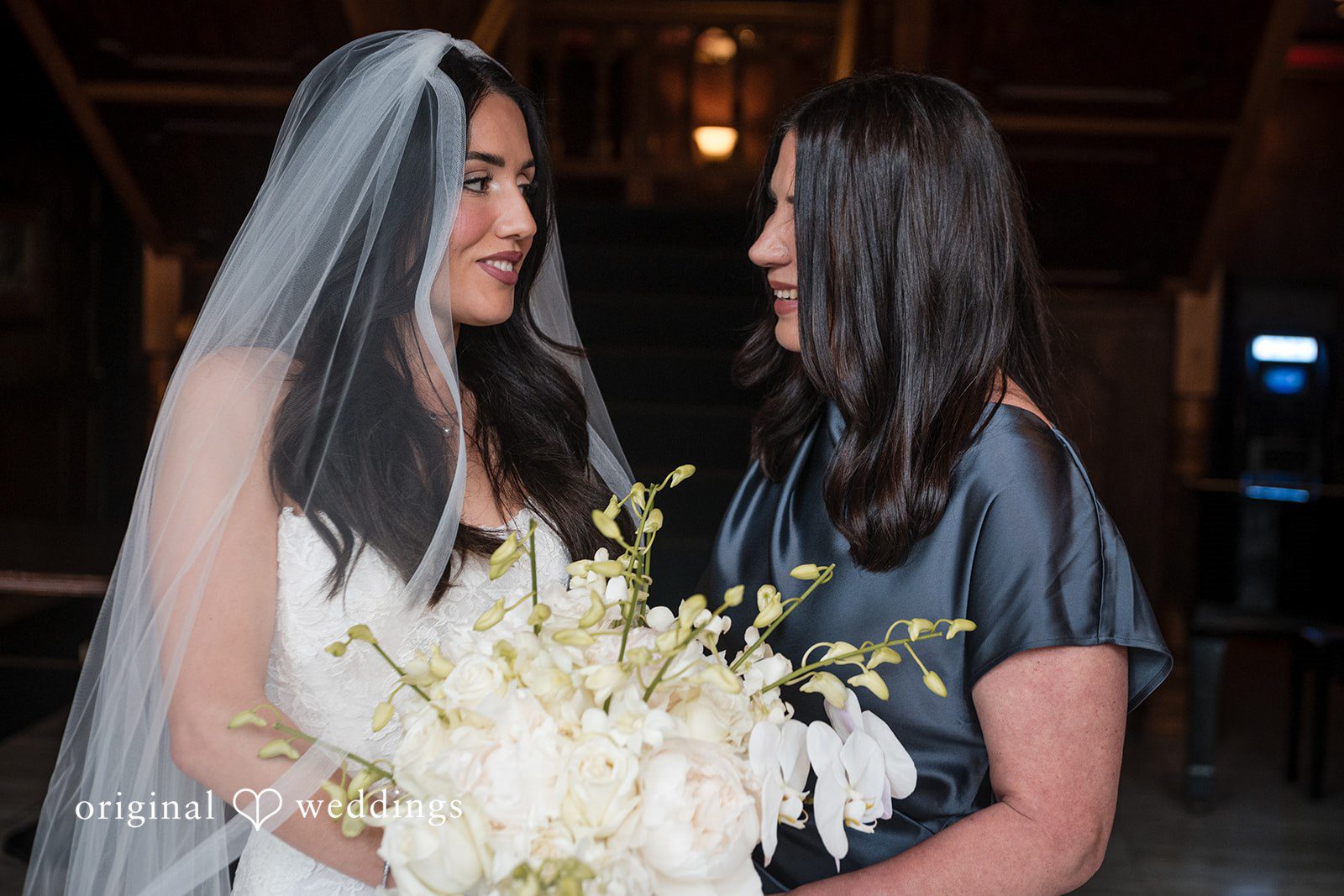 Tabatha + Justin Bride wearing a veil and one a dark robe, look at each other.