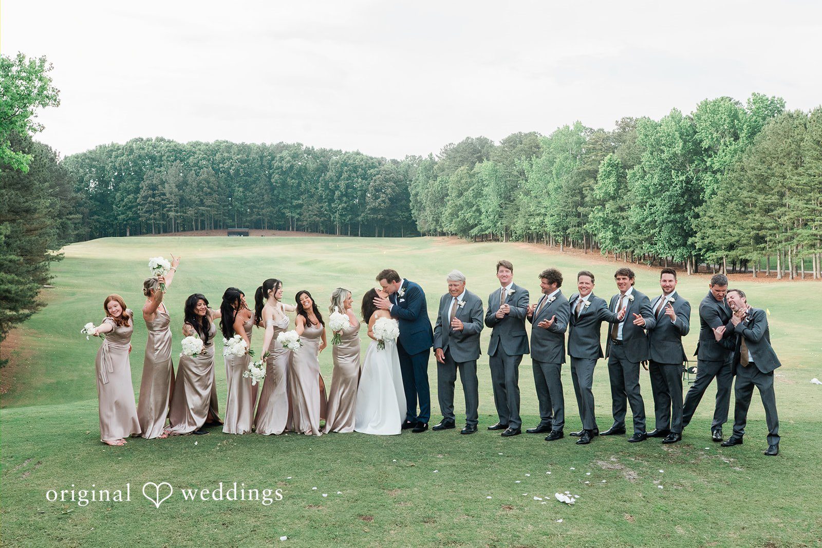 Anna + Blake Group photo of couple sharing a romantic kiss with the bridesmaids and groomsmen cheering