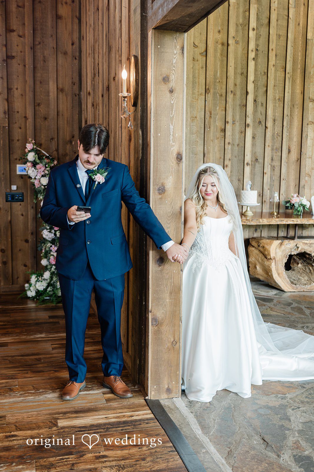 Bride and groom holding hands from opposite sides of a large barn doorway.