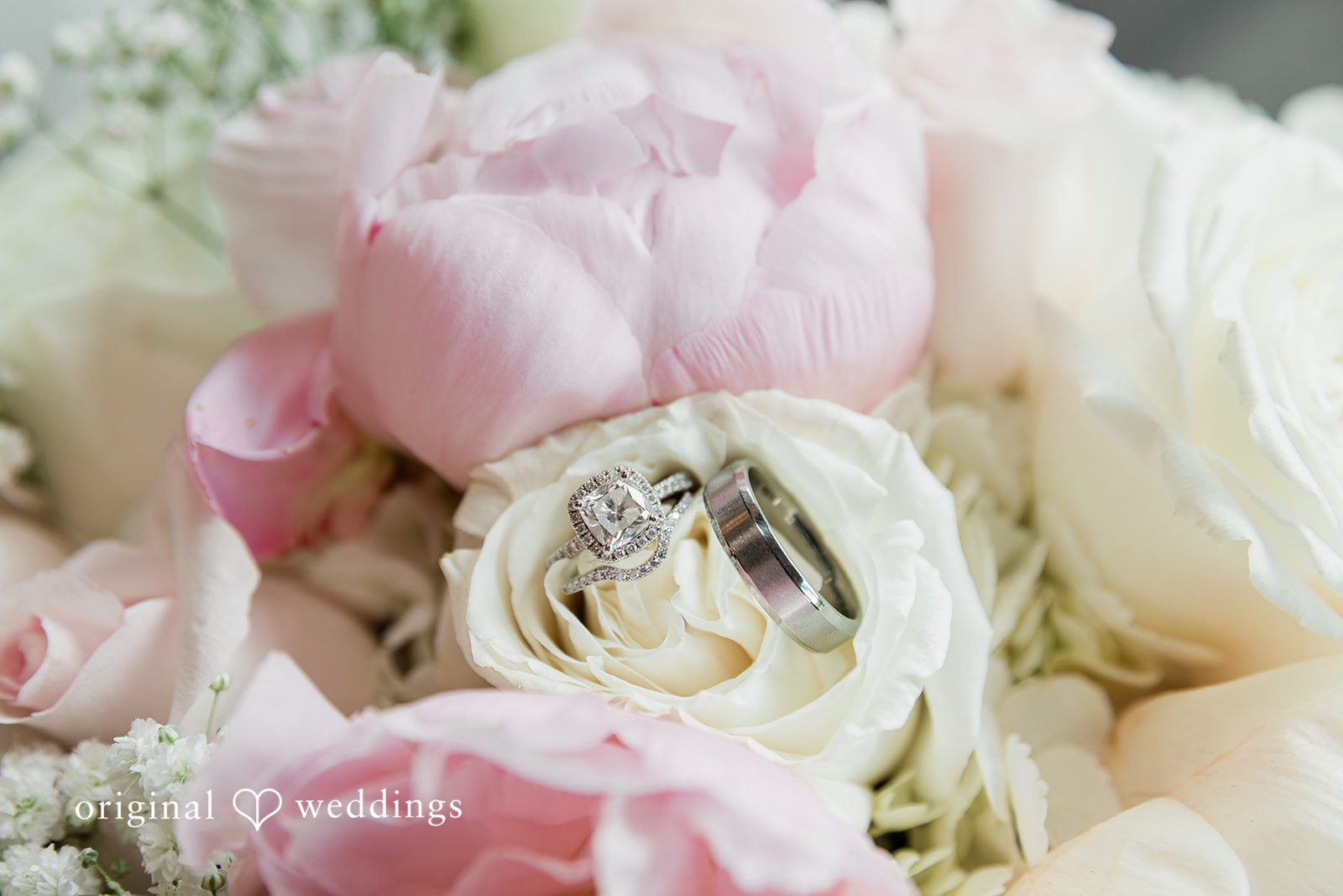Close-up detail shot of a wedding ring nestled among light pink and white peony petals.