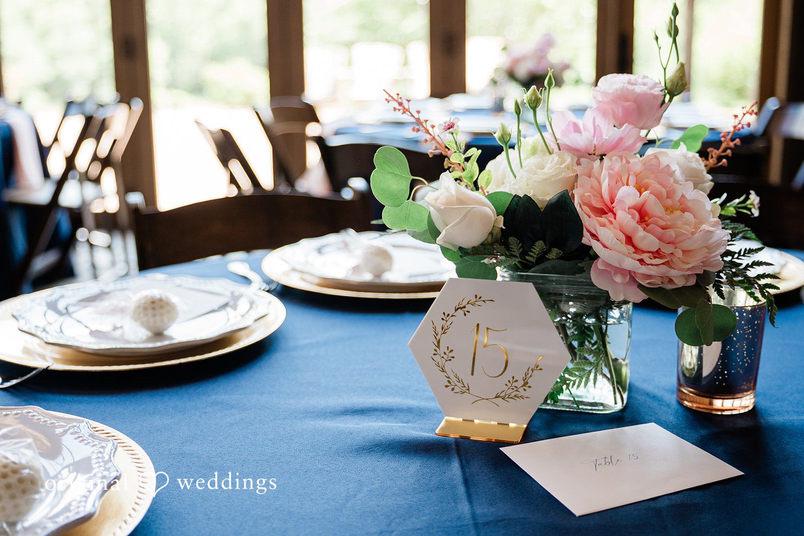 Close-up of a wedding table setting featuring a navy tablecloth, pink floral centerpiece, and a table number card.